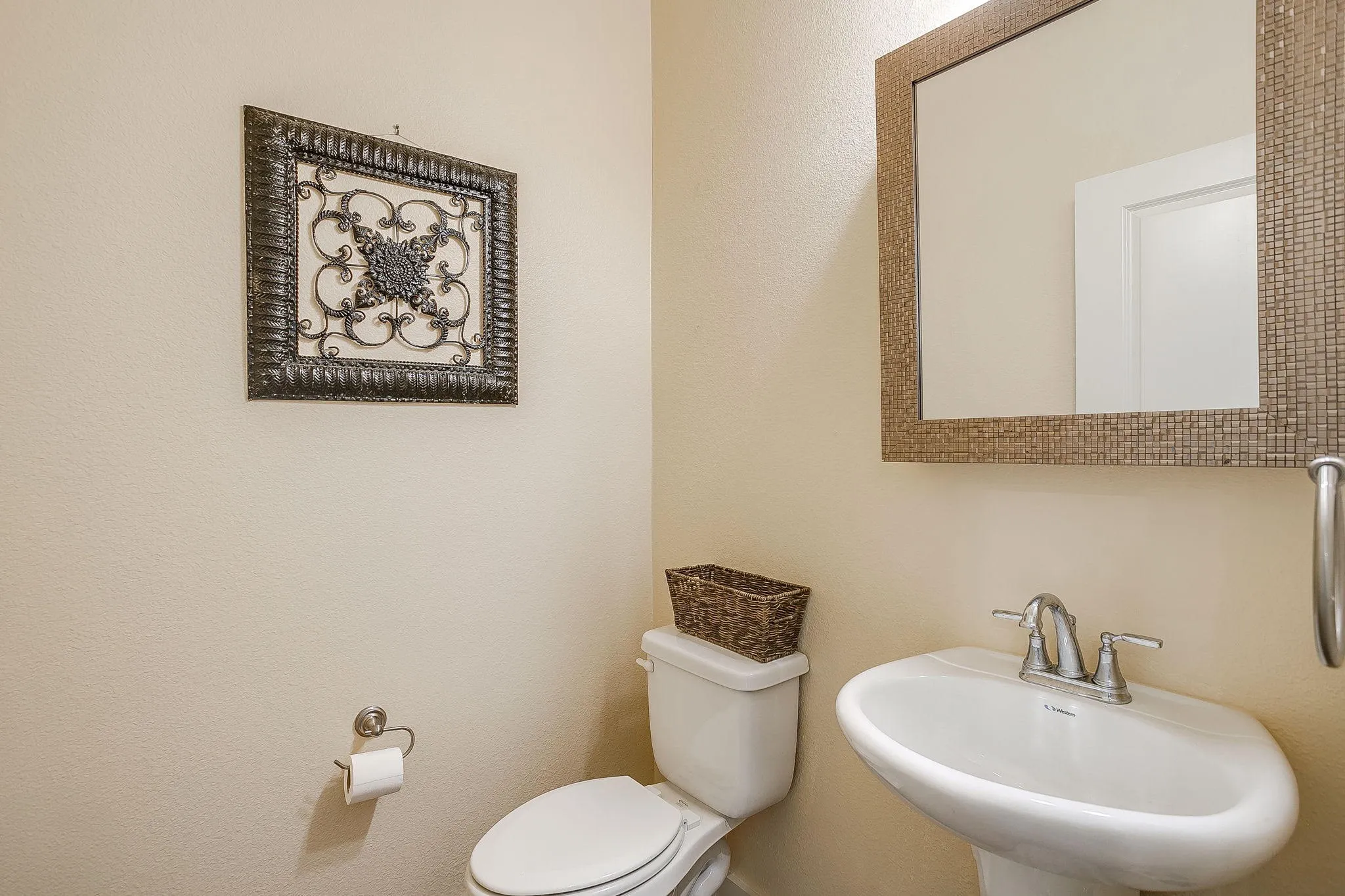 Half bath pedestal sink with a dual-handle faucet, a rectangular mirror with a mosaic-tiled frame, and a white toilet