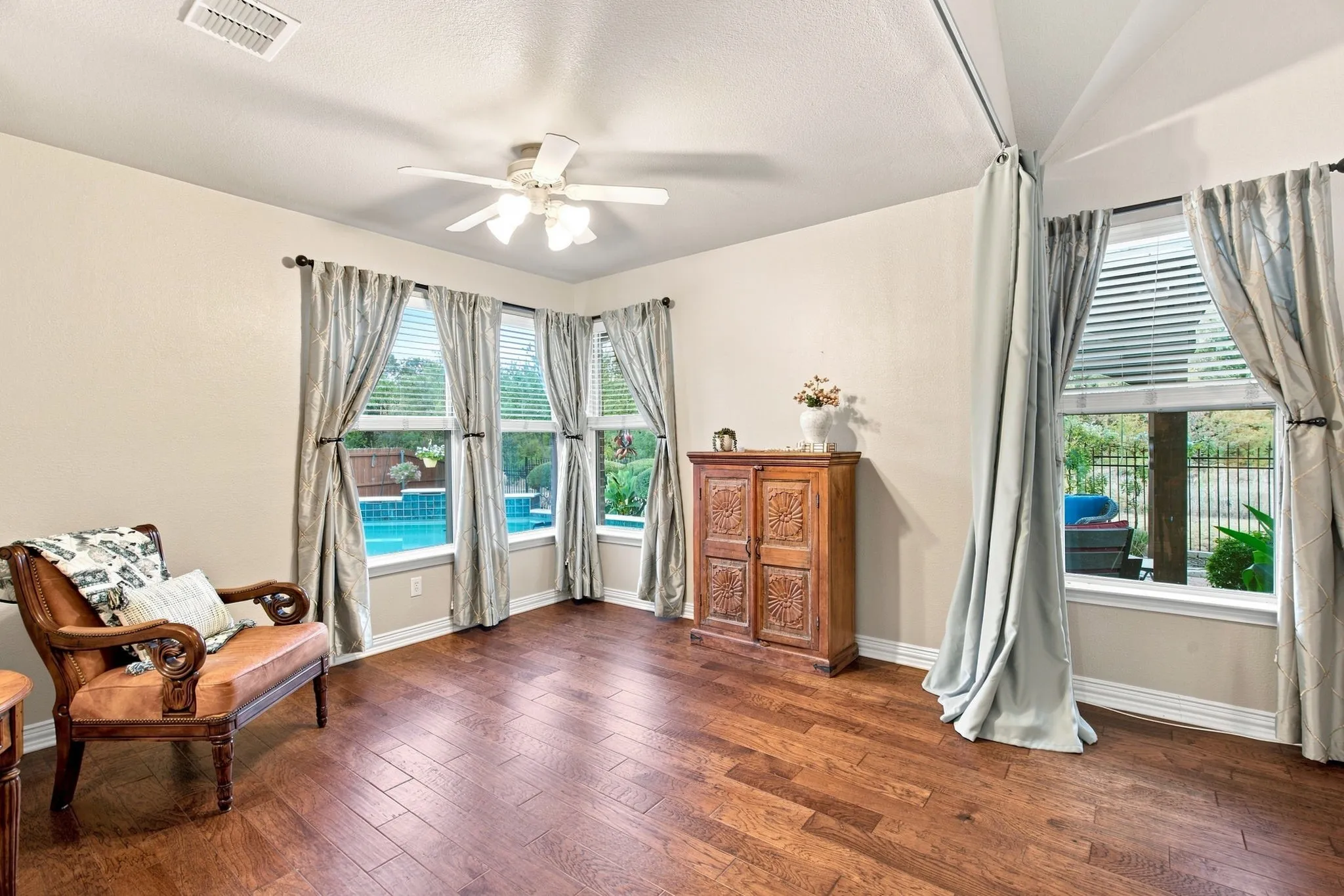 Wood-finish flooring, multiple windows with blinds, ceiling fan with light fixture, and a built-in pool visible from the interior