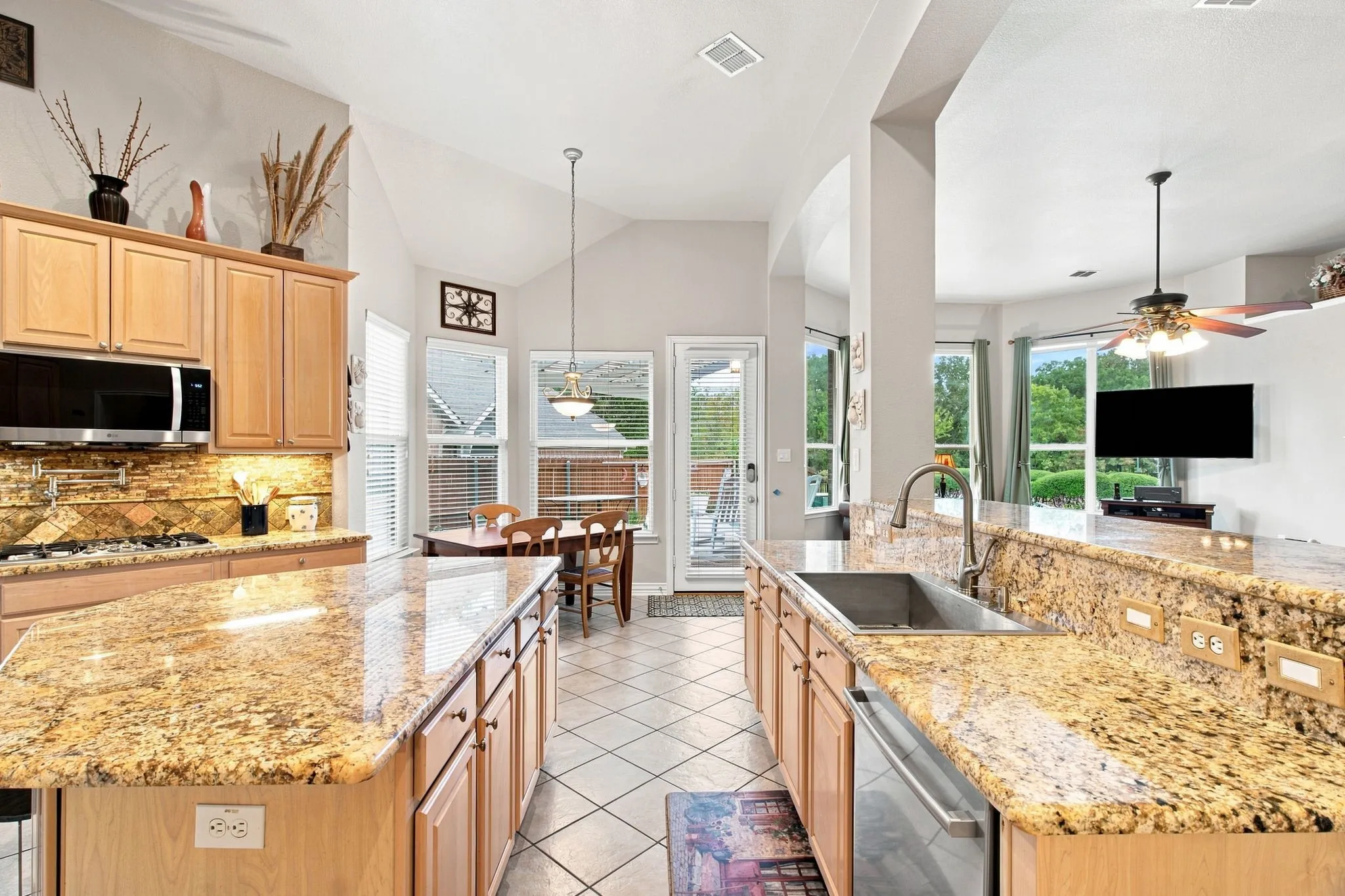 Kitchen featuring light wood cabinetry, granite countertops, tile backsplash, stainless steel appliances, and a vaulted ceiling