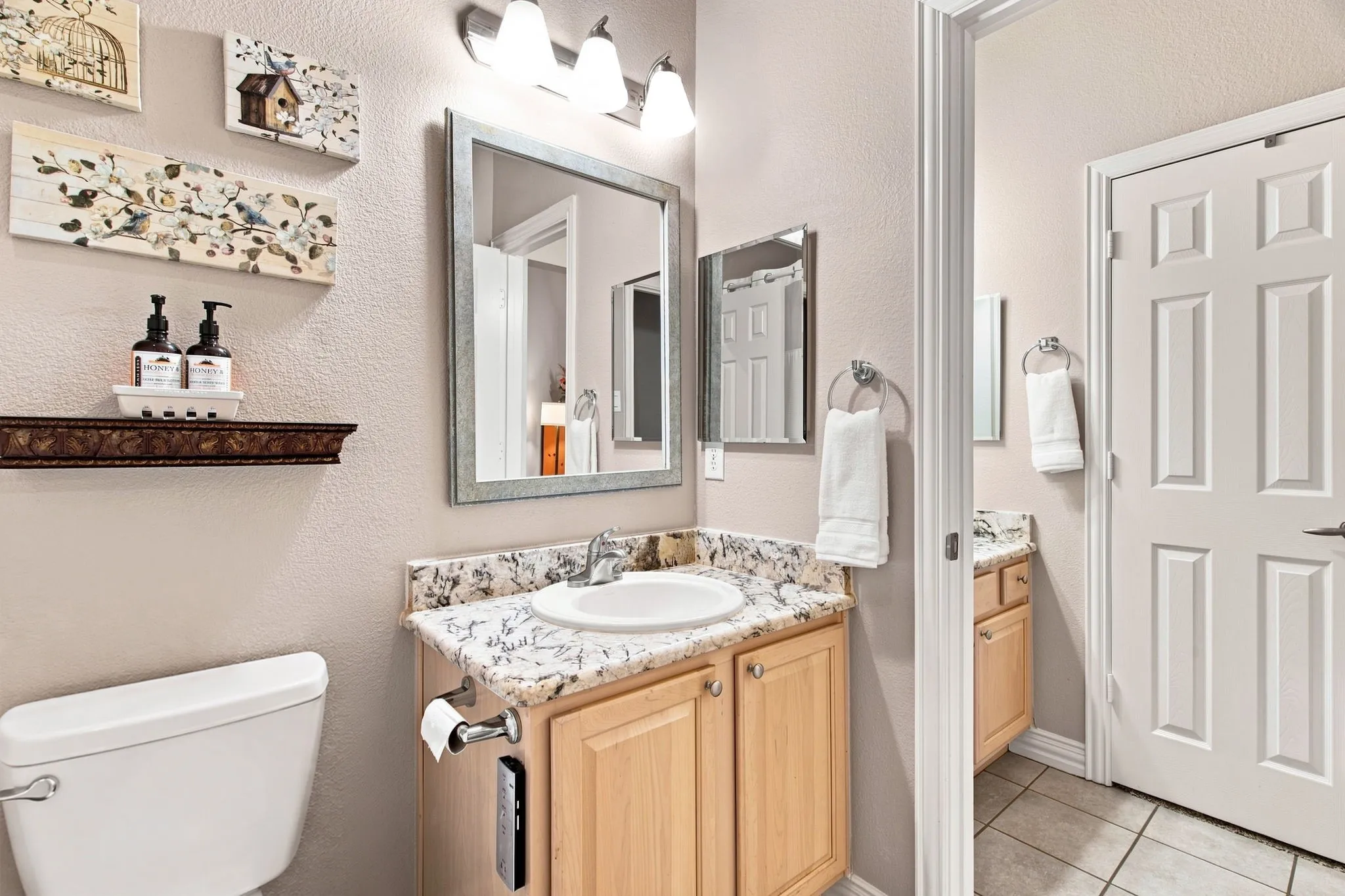 Bathroom vanity with a granite-style countertop, undermount sink, and light wood-finish cabinetry