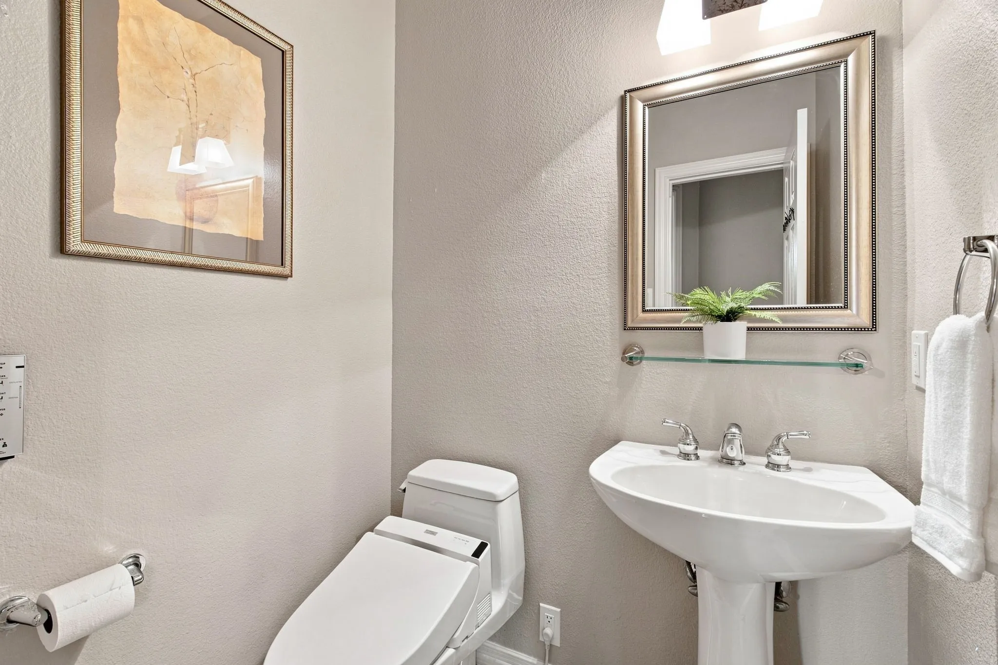 Pedestal sink with chrome fixtures, framed mirror with integrated lighting, and a glass shelf