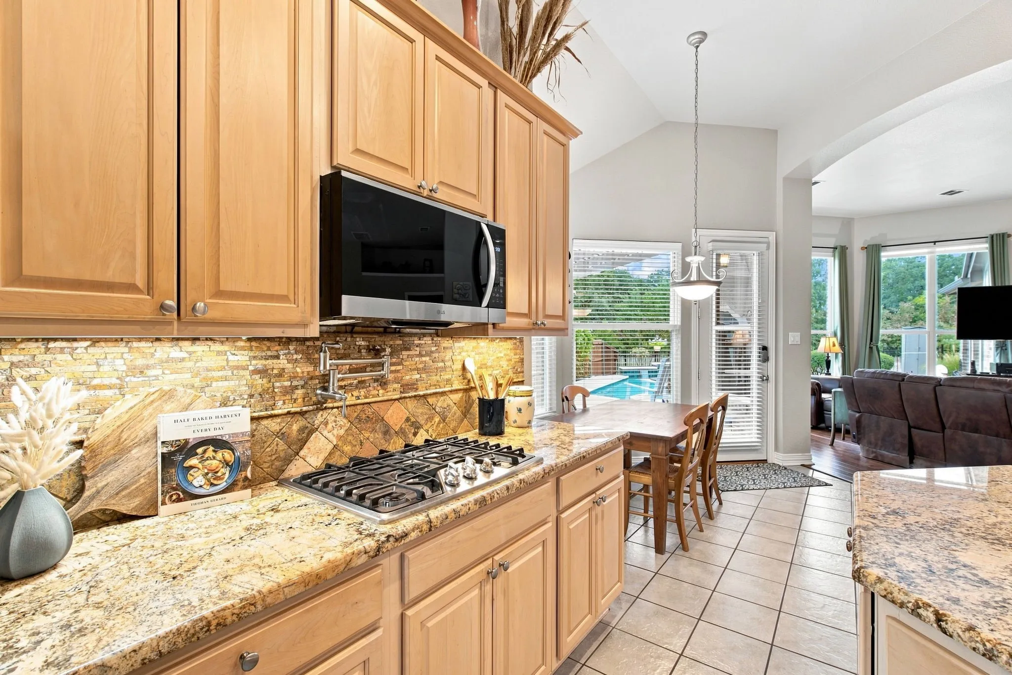 Kitchen featuring light wood cabinetry, granite countertops, tile backsplash, a built-in microwave, and a gas range