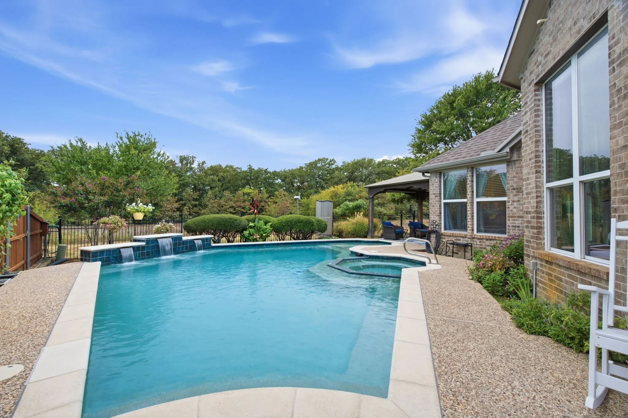 Swimming pool with integrated spa and water features, surrounded by exposed aggregate concrete and a brick exterior