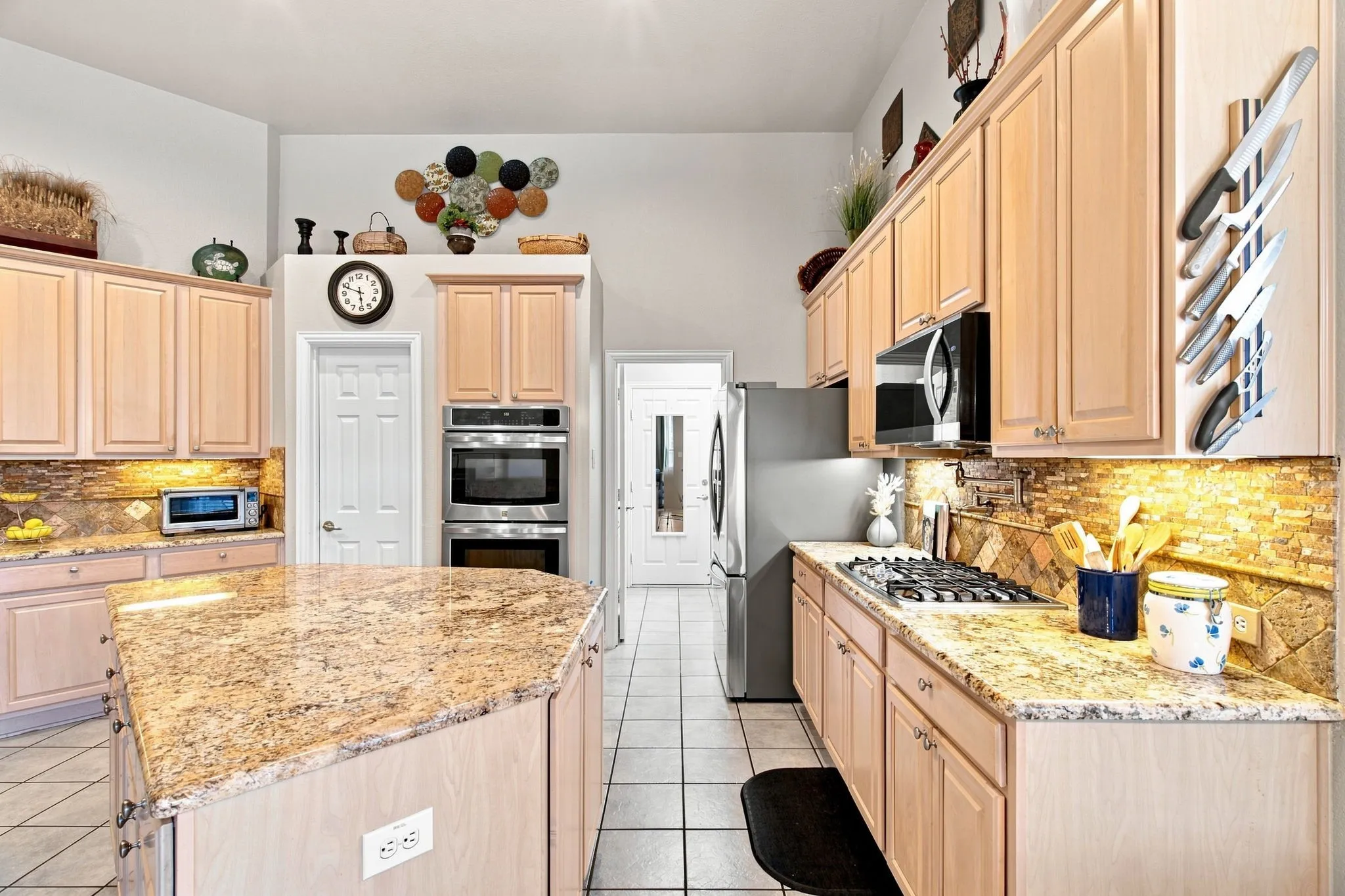 Kitchen featuring light wood cabinetry, stone countertops, stainless steel appliances, and tile flooring