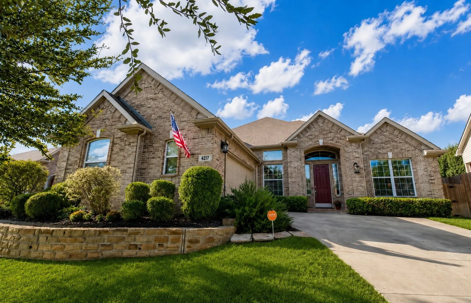Brick exterior with stone accents, arched entryway, extensive landscaping with stone retaining wall, and a concrete driveway