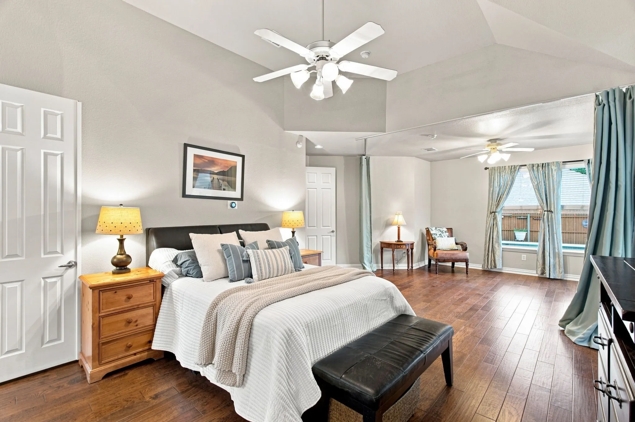 Vaulted ceiling with multiple ceiling fans, wood-finish flooring, large window with window seat, and paneled interior doors