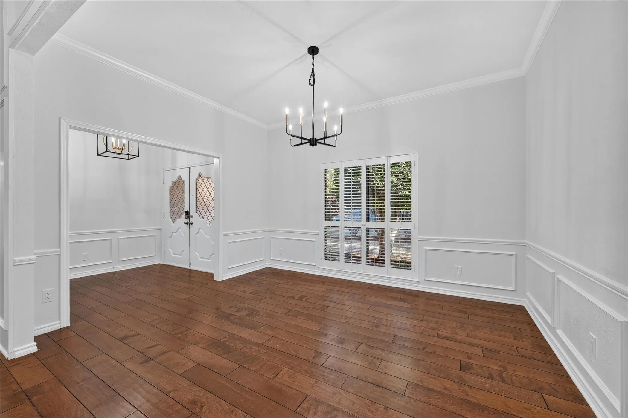 Vaulted ceiling with a black finish chandelier, wood-finish flooring, and white wainscoting