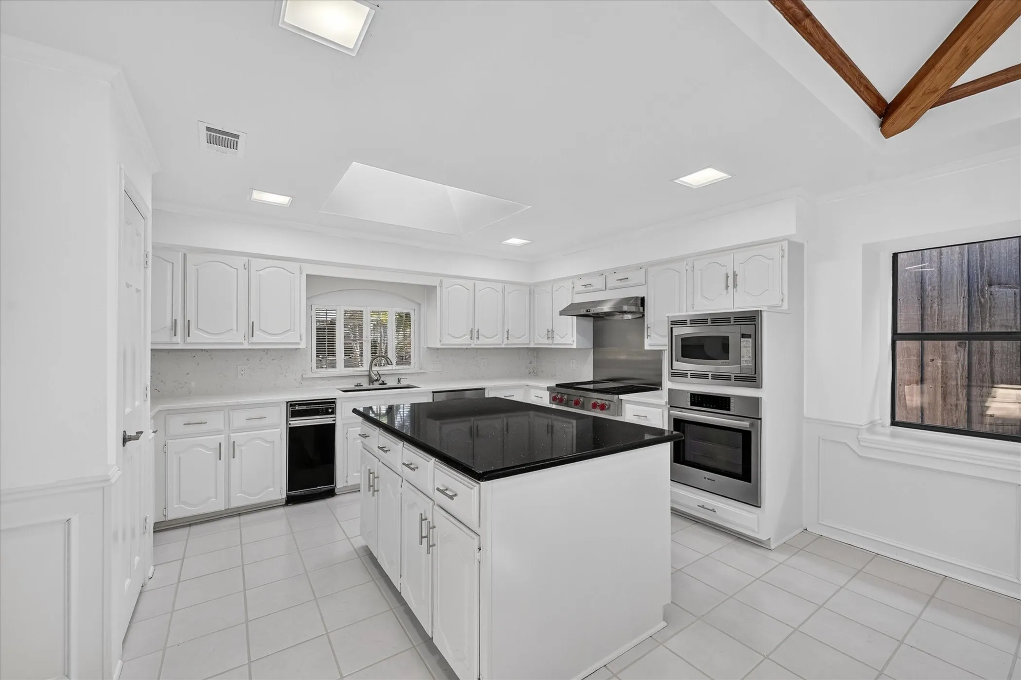 Bright kitchen featuring white cabinetry, a central island with a dark countertop, stainless steel appliances, and tile flooring