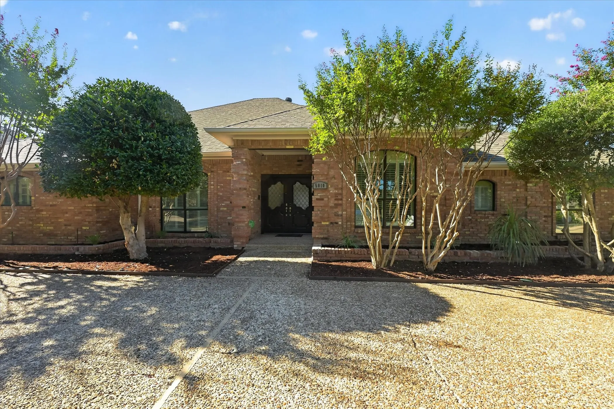 Brick exterior, gabled roofline, double entry doors, arched windows, and a gravel driveway