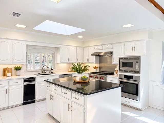 staged white cabinetry, stainless steel appliances, granite island countertop, white tile flooring, and a skylight