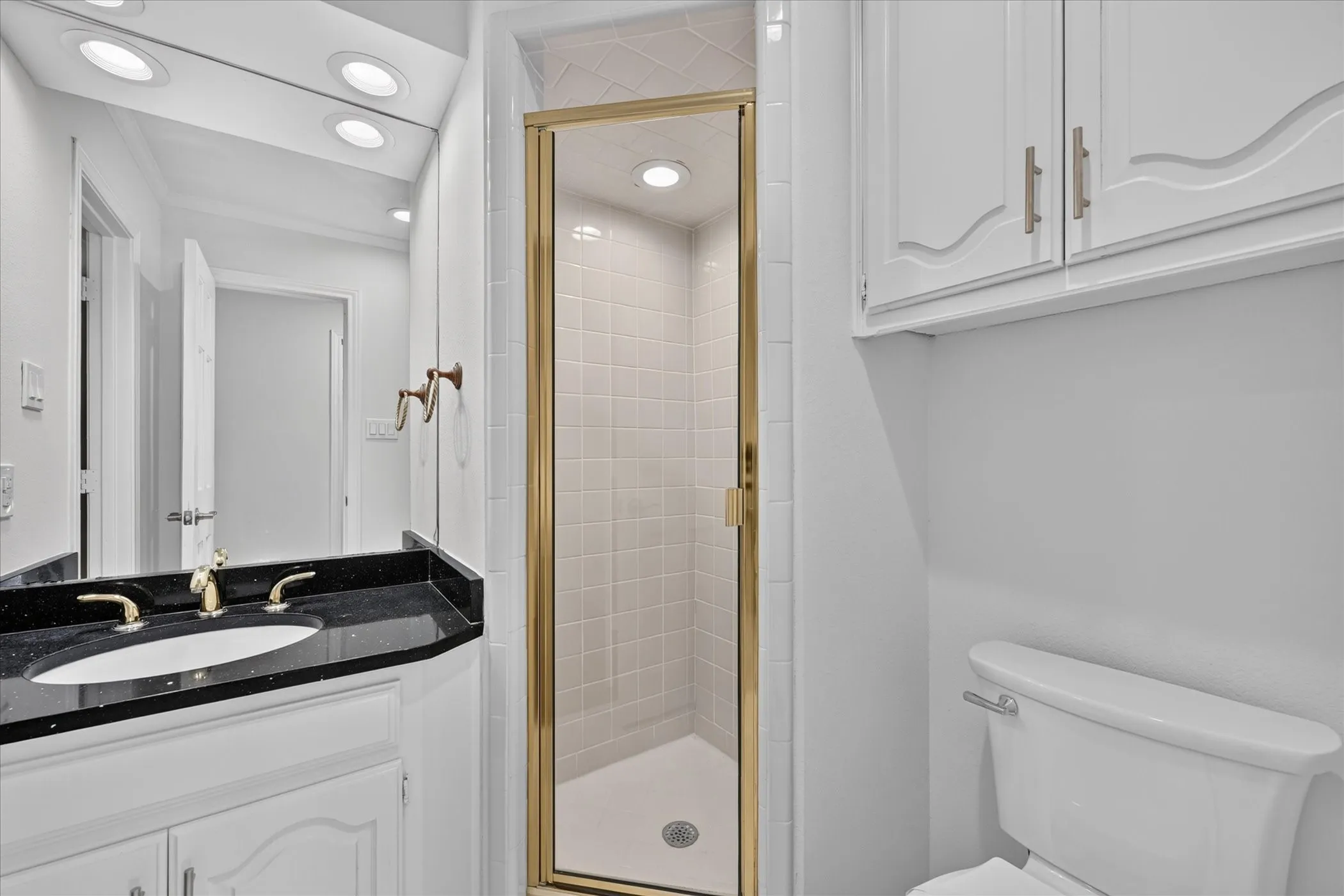  3rd Bathroom featuring a walk-in shower with gold-toned framing, a white vanity with a black countertop, integrated sink, and gold-toned fixtures off 1st bedroom or study