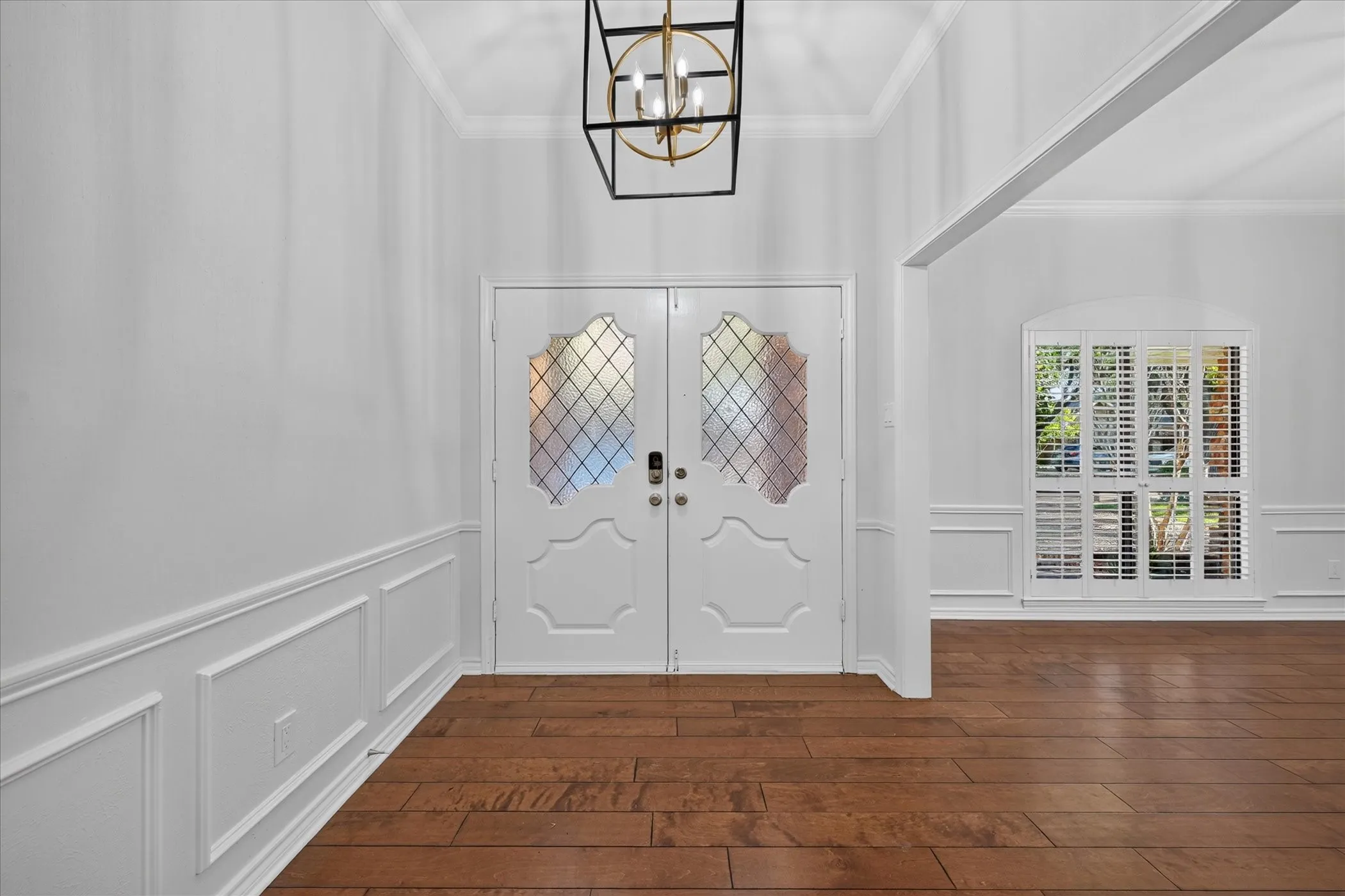 Double entry doors with decorative glass panels, wood-finish flooring, wainscoting, crown molding, and a contemporary ceiling fixture