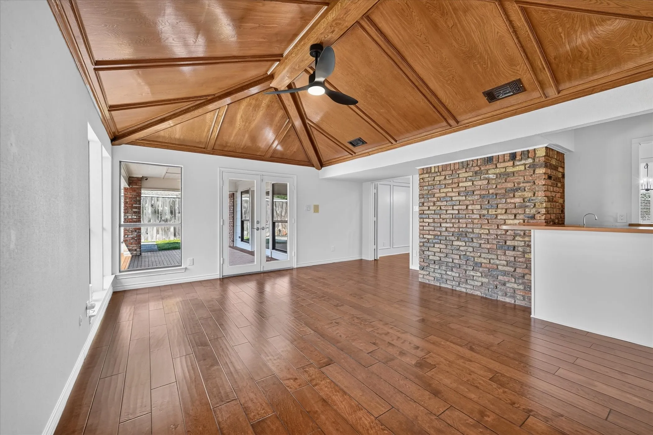 Vaulted wood-finish ceiling with exposed beams, wood-finish flooring, brick accent wall, double French doors, and a built-in bar