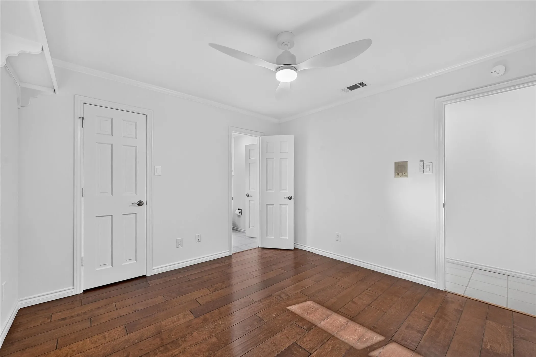 Wood-finish flooring, ceiling fan with integrated lighting, white paneled doors, and crown molding