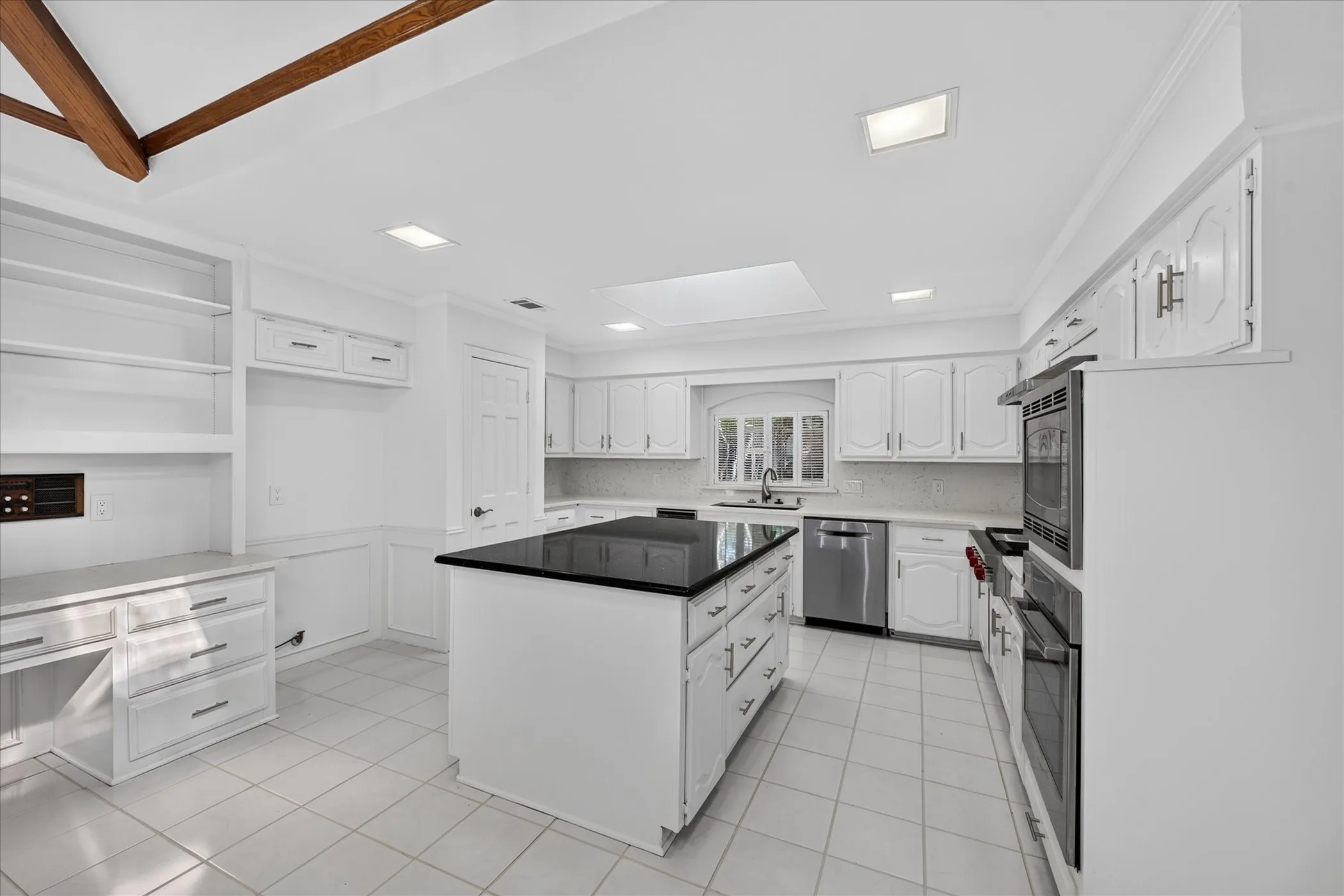 White cabinetry, stainless steel appliances, central island with dark countertop, tile flooring, and built-in desk with shelving