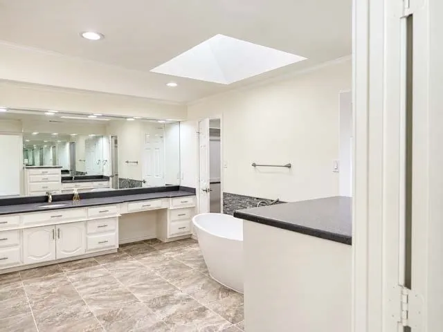 Spacious bathroom featuring a large skylight, an expansive vanity with double sinks, a freestanding bathtub, and tiled flooring