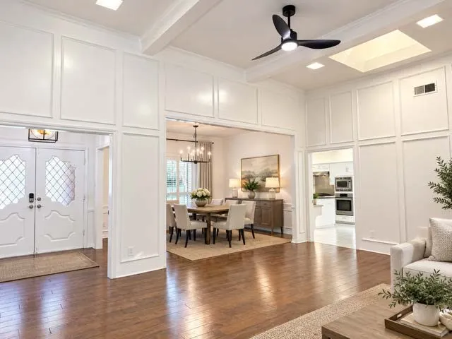 staged Hardwood flooring, decorative wall paneling, ceiling fan with integrated lighting, skylight, and recessed lighting