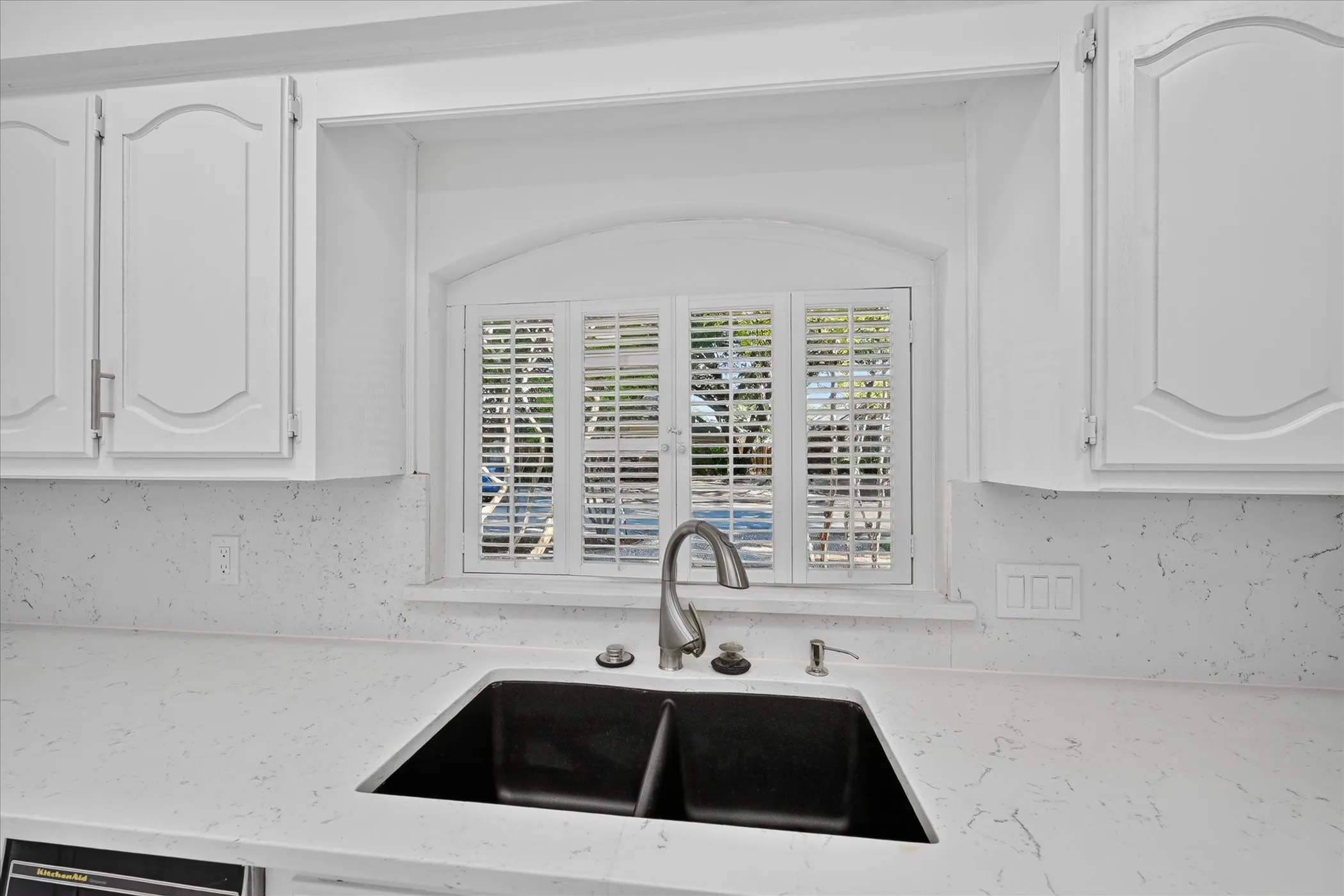 White cabinetry with decorative arch panels, light-toned countertops, and a black undermount double sink with a gooseneck faucet