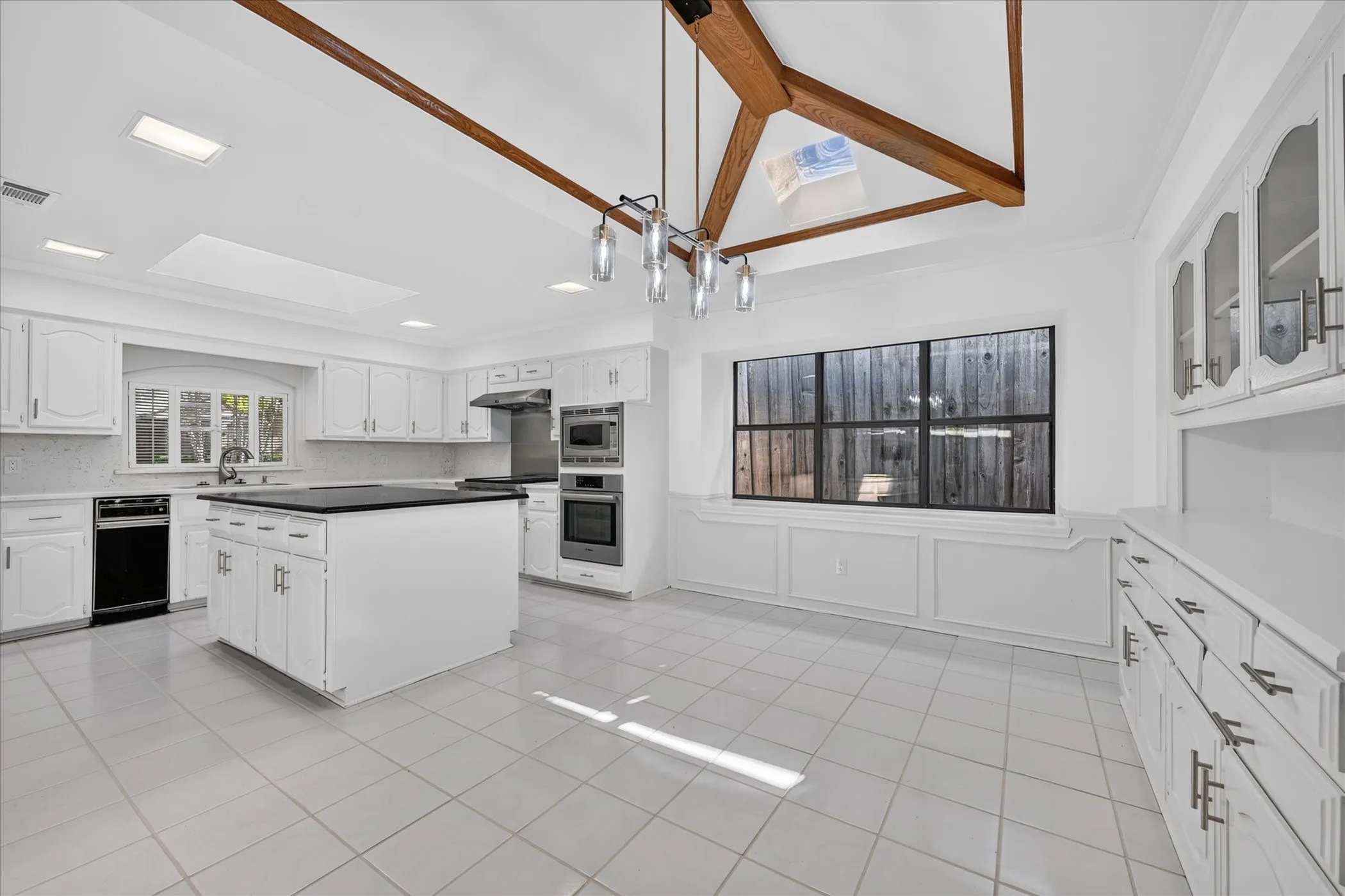 Vaulted ceiling with exposed wood beams, white cabinetry, dark countertops, built-in appliances, and tile flooring