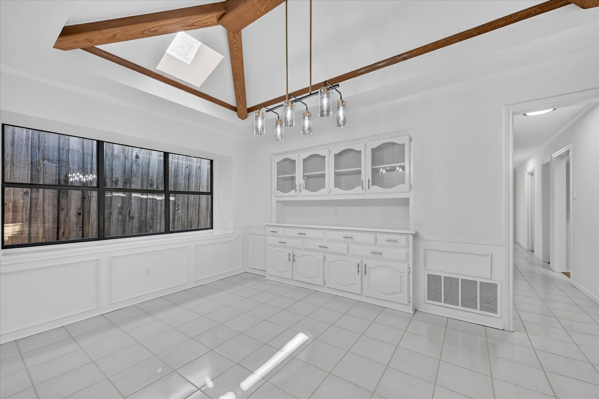 Vaulted ceiling with exposed wood beams, skylight, and decorative chandelier