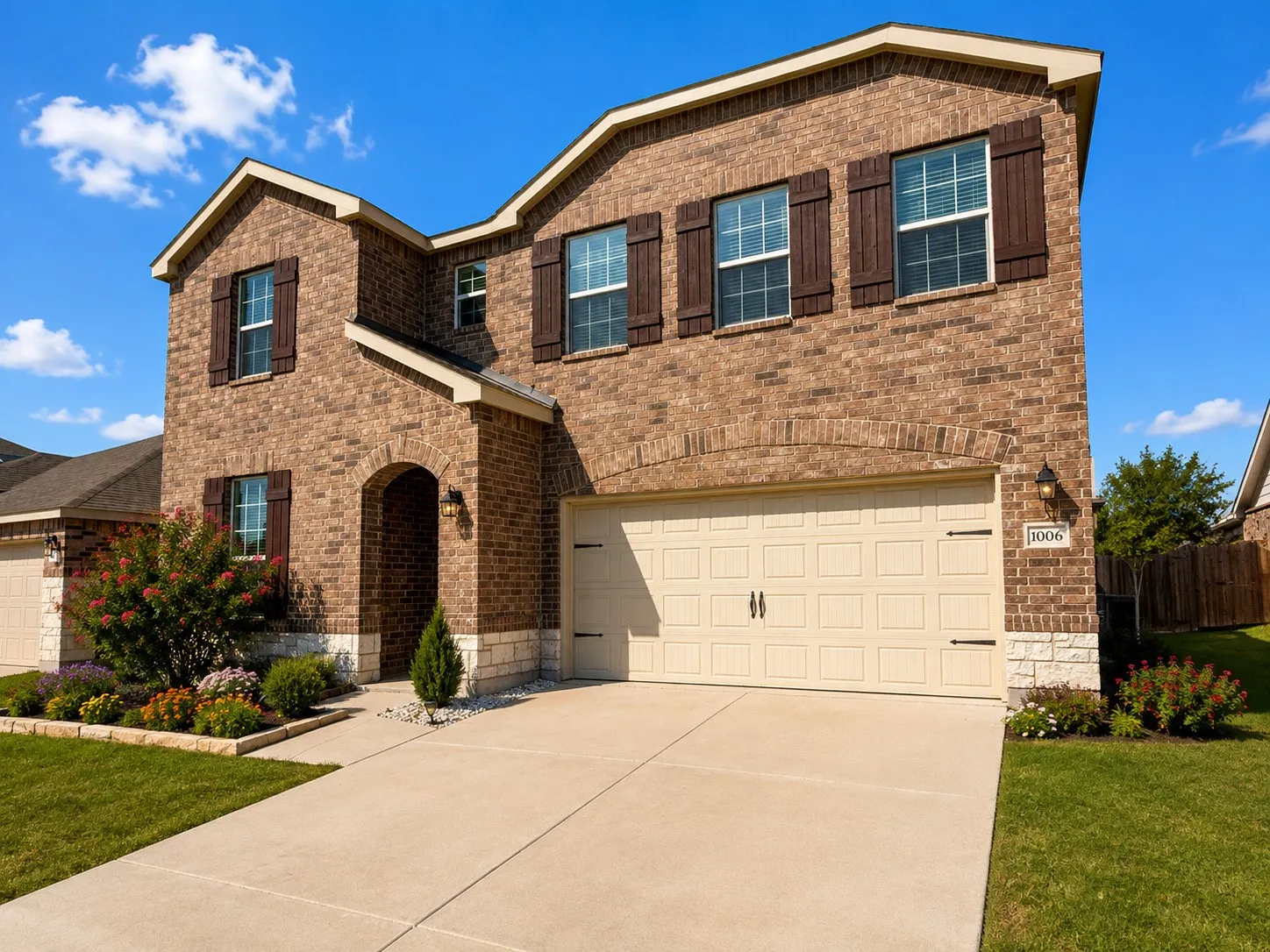 Brick exterior with stone accents, arched entry, two-car garage, manicured landscaping, and dark shutters