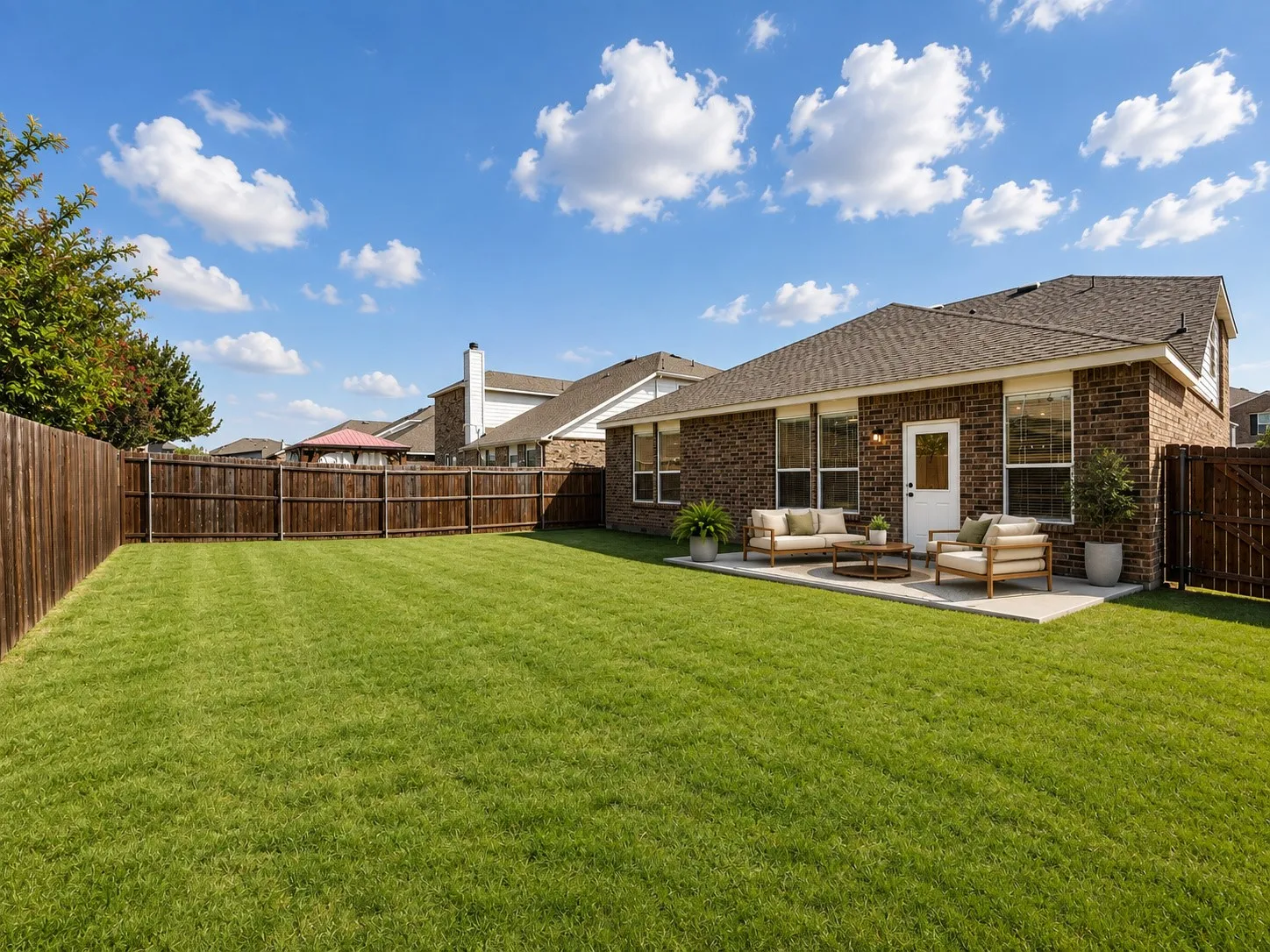 Expansive green lawn with a privacy fence, brick exterior, and a concrete patio