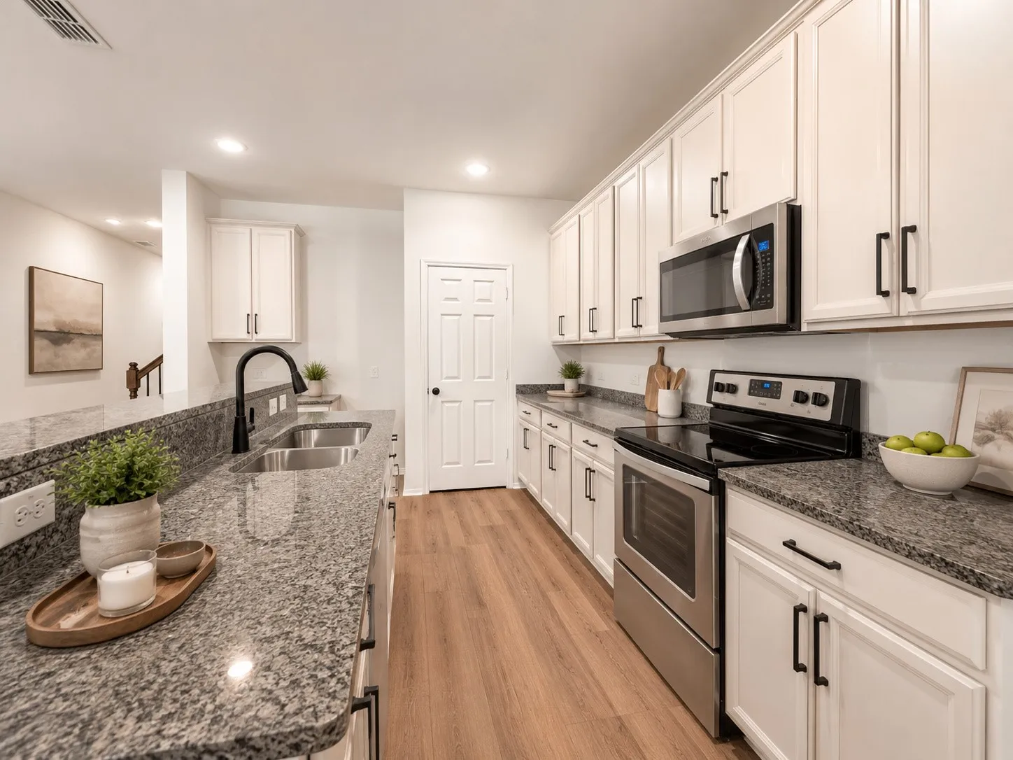 White cabinetry, stainless steel appliances, granite countertops, wood-finish flooring, and recessed lighting