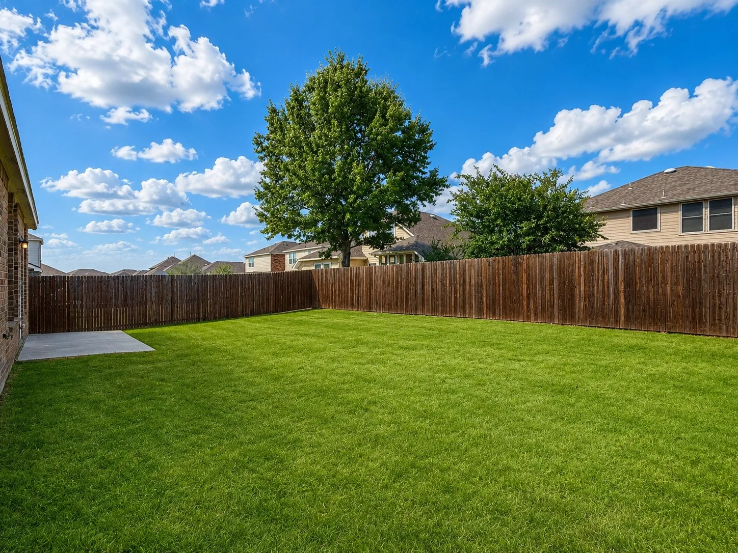 Expansive lawn with a wooden privacy fence, mature trees, and a concrete patio