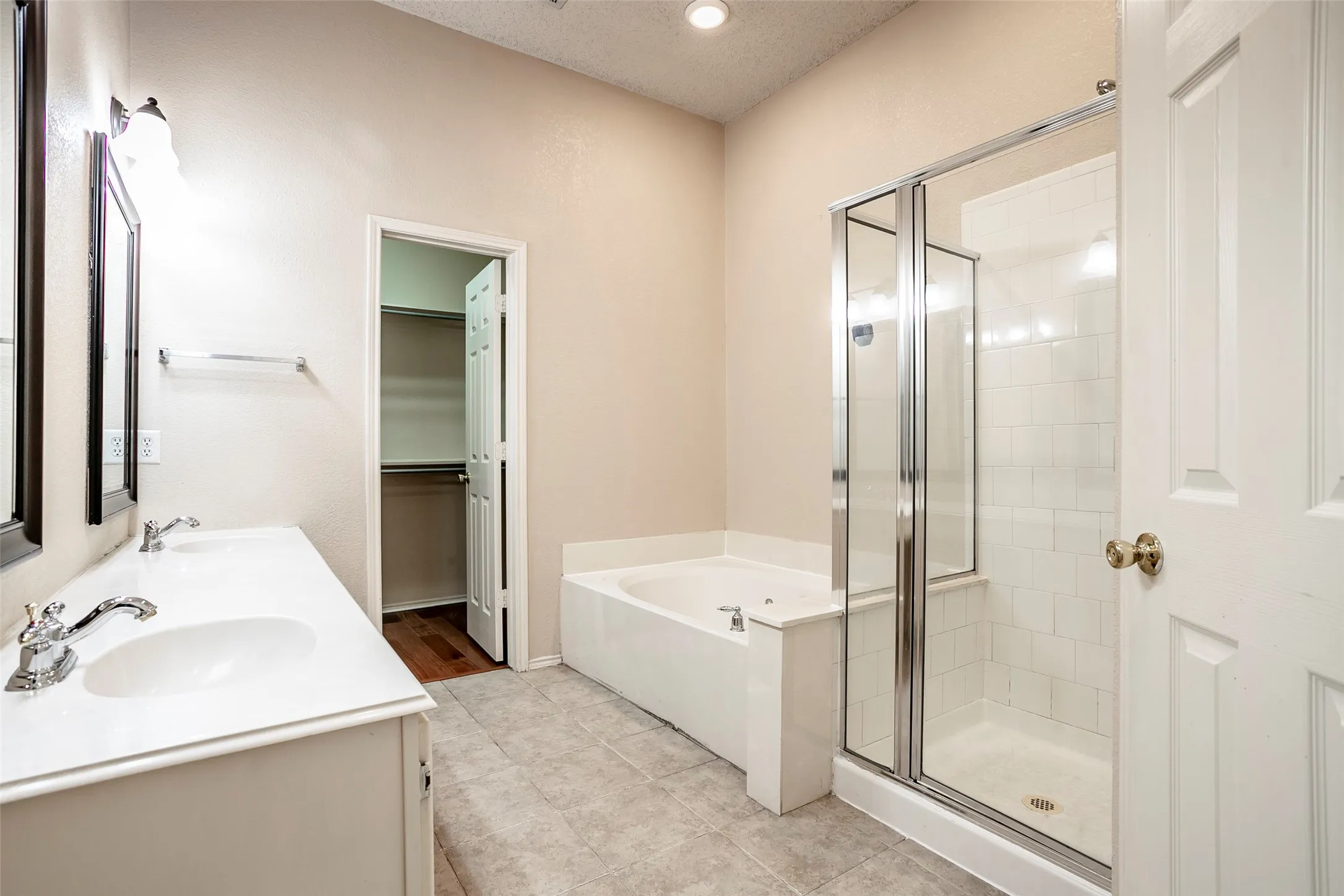 Dual vanity with integrated sinks, framed mirrors, a built-in bathtub, a walk-in shower with clear glass enclosure, and tile flooring
