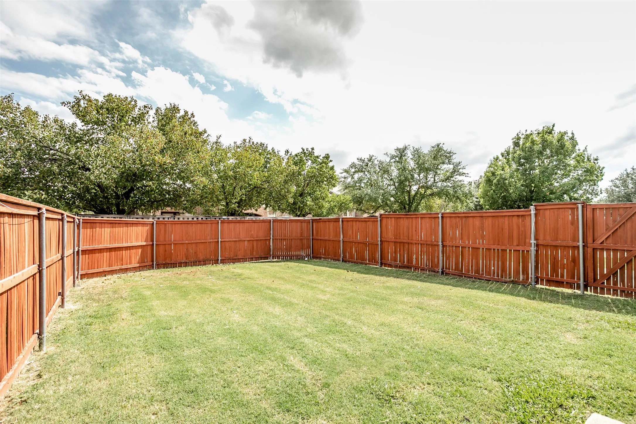 Expansive backyard featuring a manicured lawn, full privacy fencing, and a wooden gate