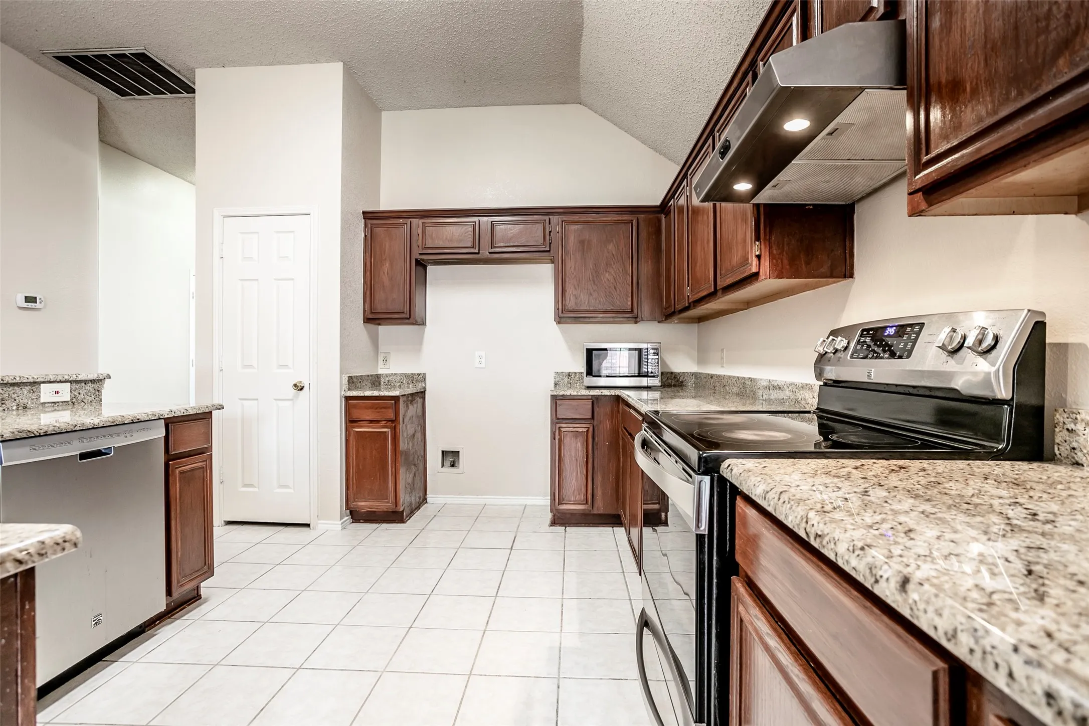 Kitchen featuring granite countertops, wood cabinetry, stainless steel range with overhead ventilation, and tile flooring