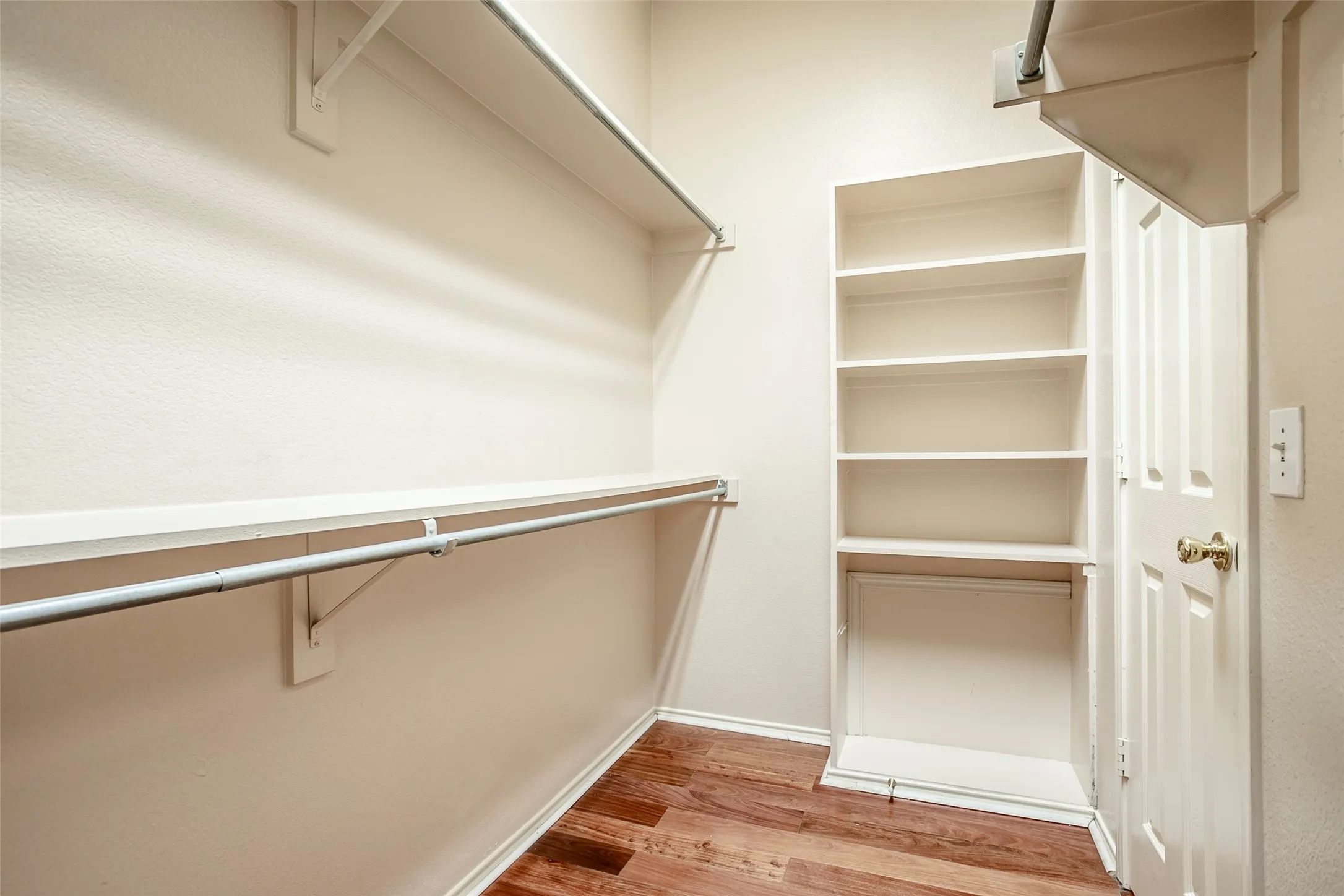 Walk-in closet featuring wood-finish flooring, built-in shelving, and multiple hanging rods