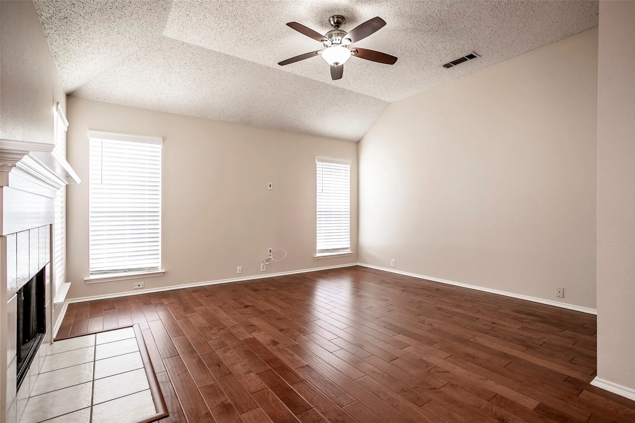 Vaulted ceiling with a ceiling fan, fireplace with a tile hearth, and dark wood-finish flooring
