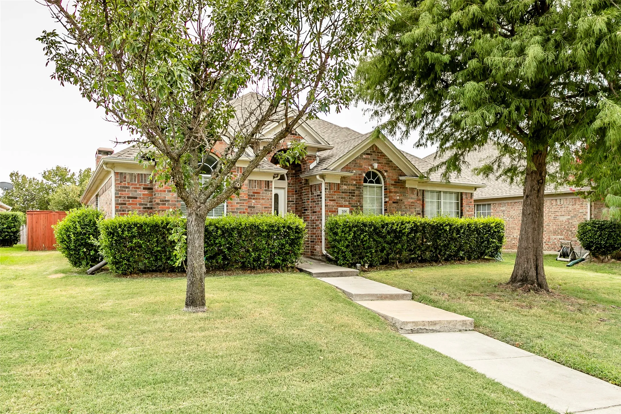 Brick exterior with arched windows, gabled roofline, concrete walkway, and mature landscaping