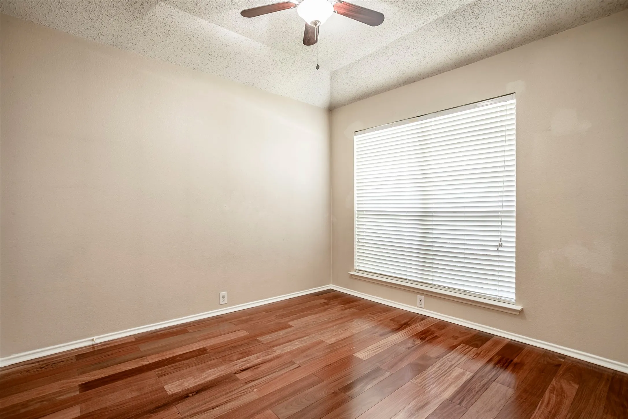 Wood-finish flooring, a large window with horizontal blinds, and a ceiling fan with integrated lighting