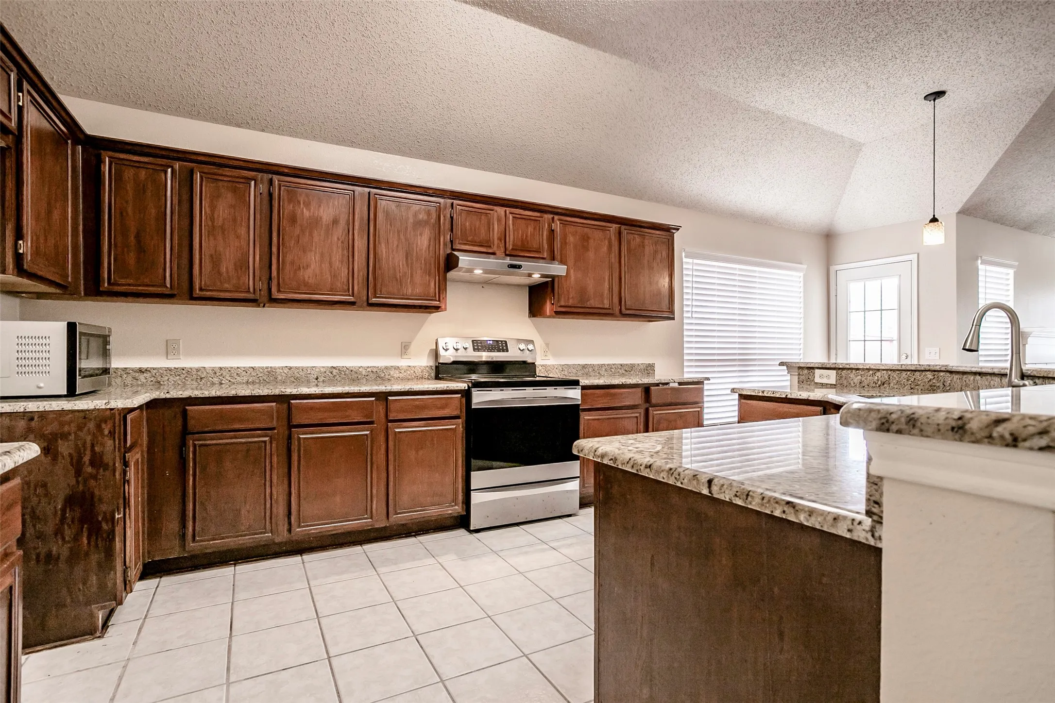 Kitchen featuring wood cabinetry, light-toned granite countertops, stainless steel appliances, and white tiled flooring