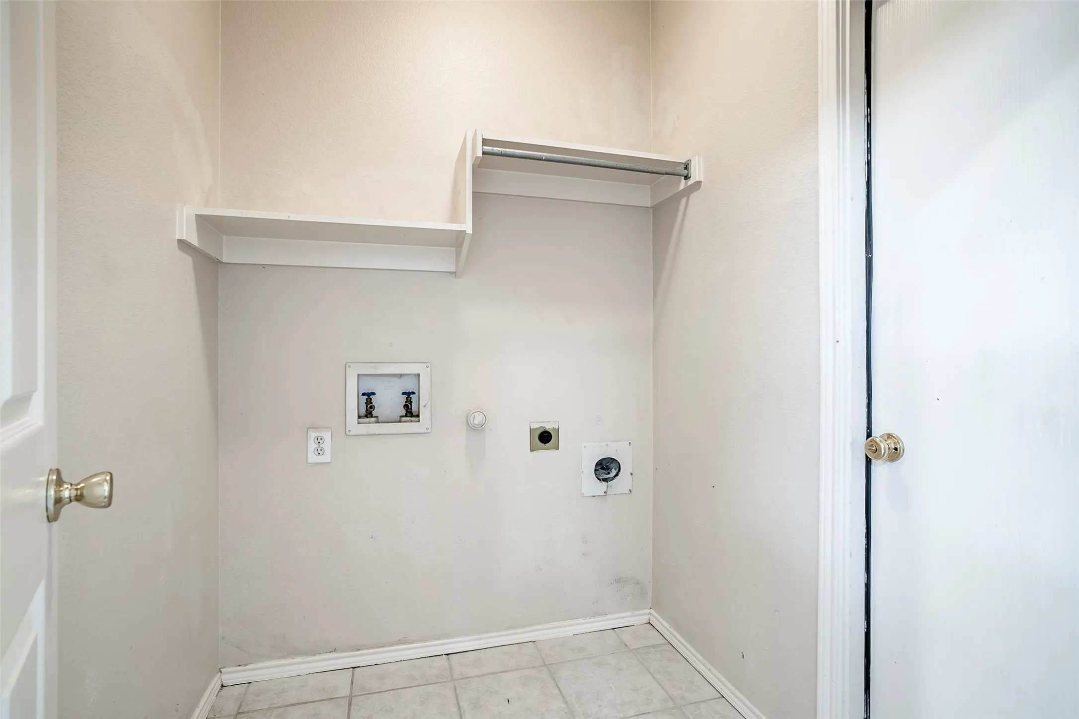 Utility area with white shelving, integrated hanging rod, and tiled flooring
