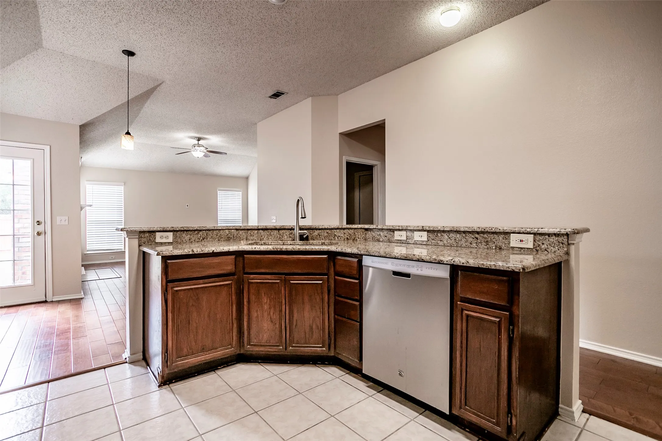 Kitchen area with a built-in dishwasher, an undermount sink, granite countertops, and wood cabinetry