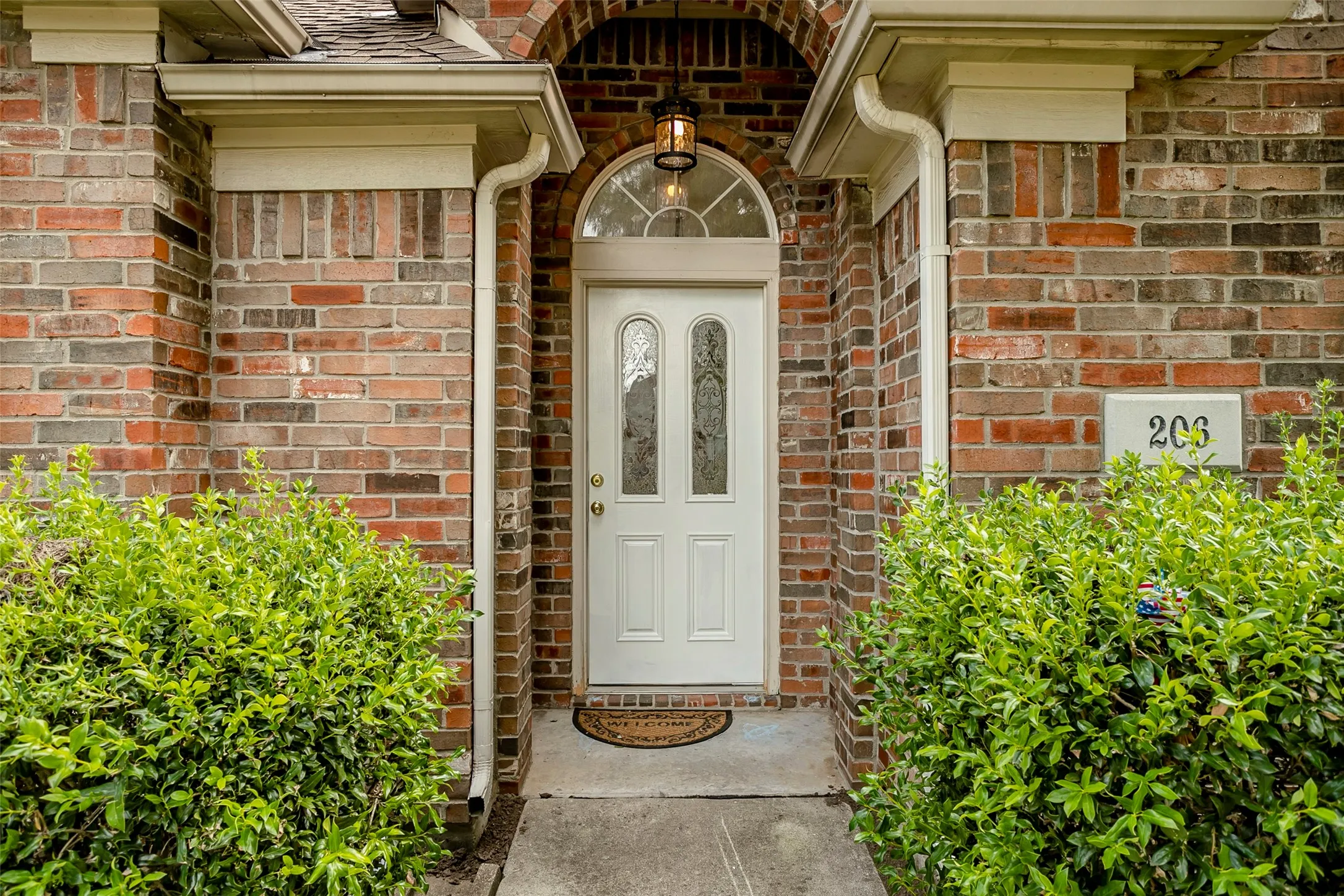 Brick exterior with a white entry door, arched transom window, and integrated overhead lighting