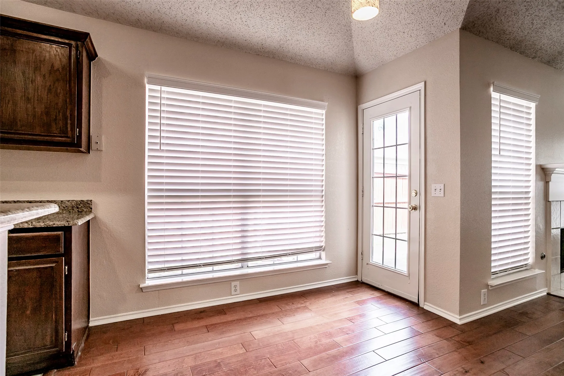 Wood-finish flooring, dark wood cabinetry, light countertop, multiple windows with blinds, and a glass-paned door
