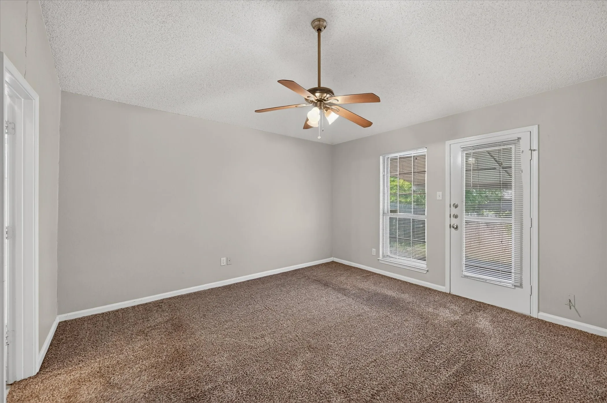 Wall-to-wall carpeting, ceiling fan with integrated lighting, window with horizontal blinds, and a glass-paneled door
