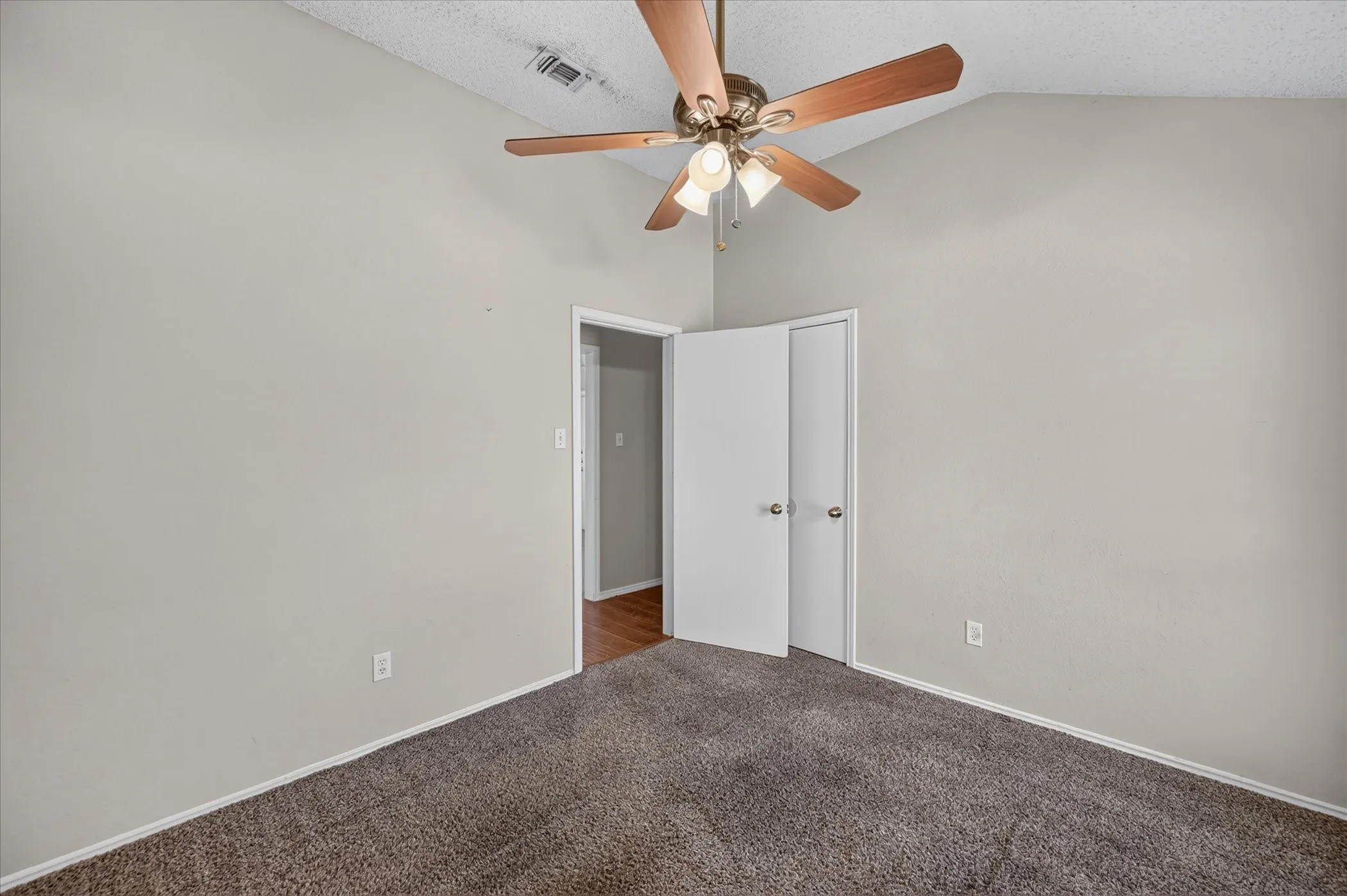 Vaulted ceiling with a ceiling fan, light gray wall paint, brown carpet flooring, and white bifold closet doors