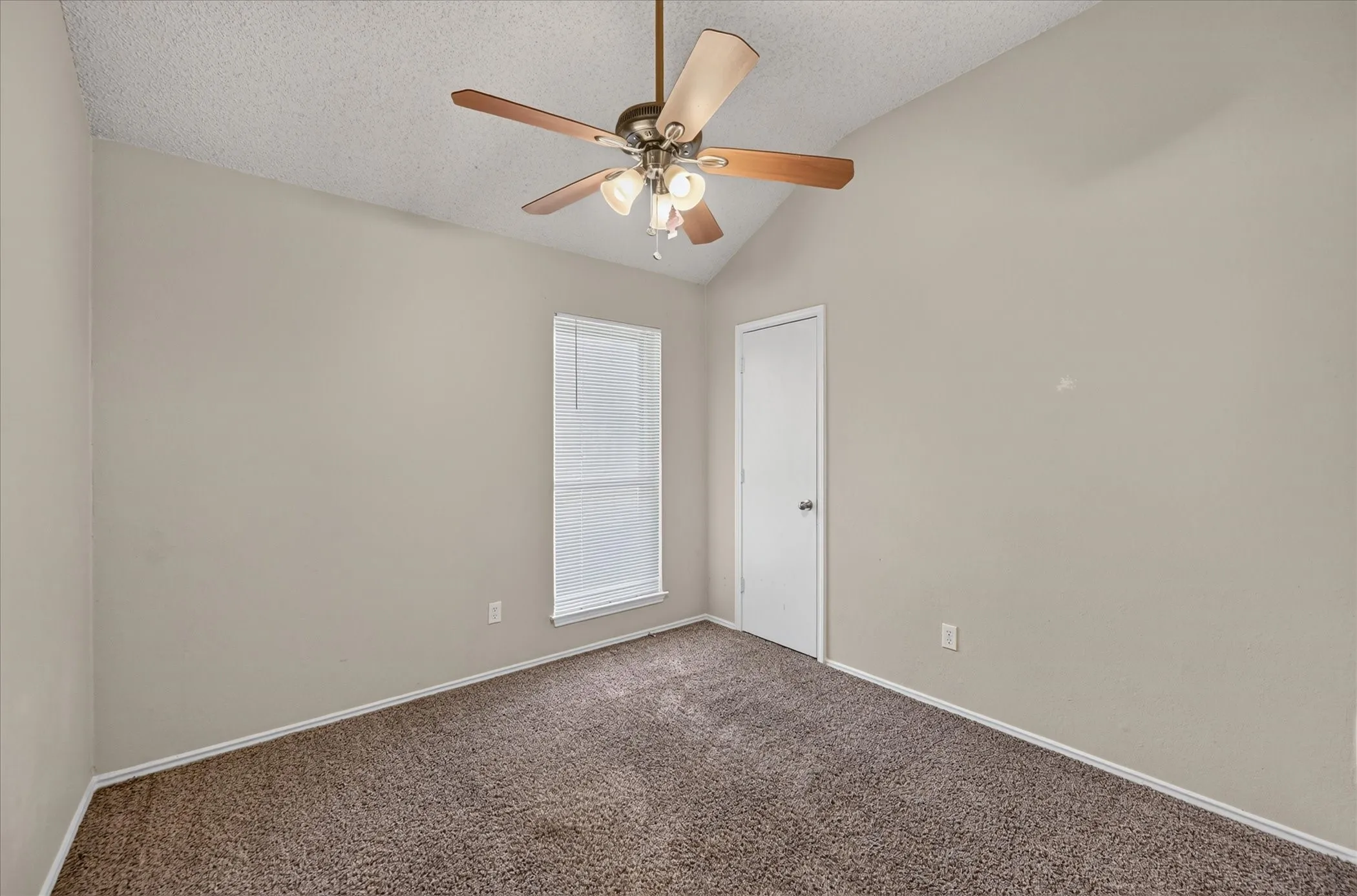 Vaulted ceiling with a ceiling fan, neutral wall color, and textured carpeting