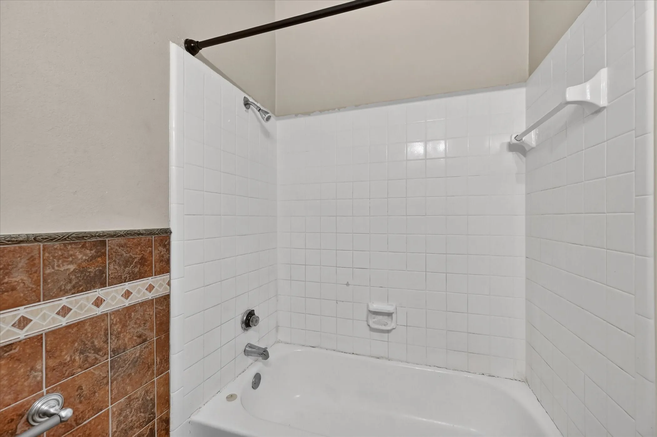 Bathtub with white tile surround, integrated soap dish, and a shower curtain rod