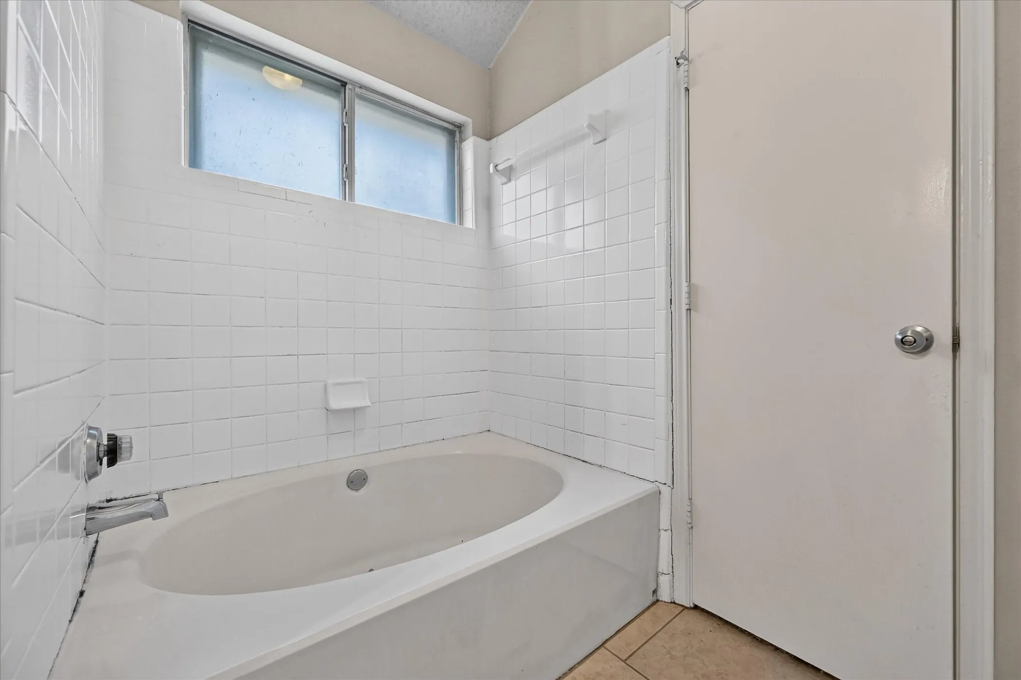 Tub-shower combination with white subway tile surround, polished chrome fixtures, and frosted window