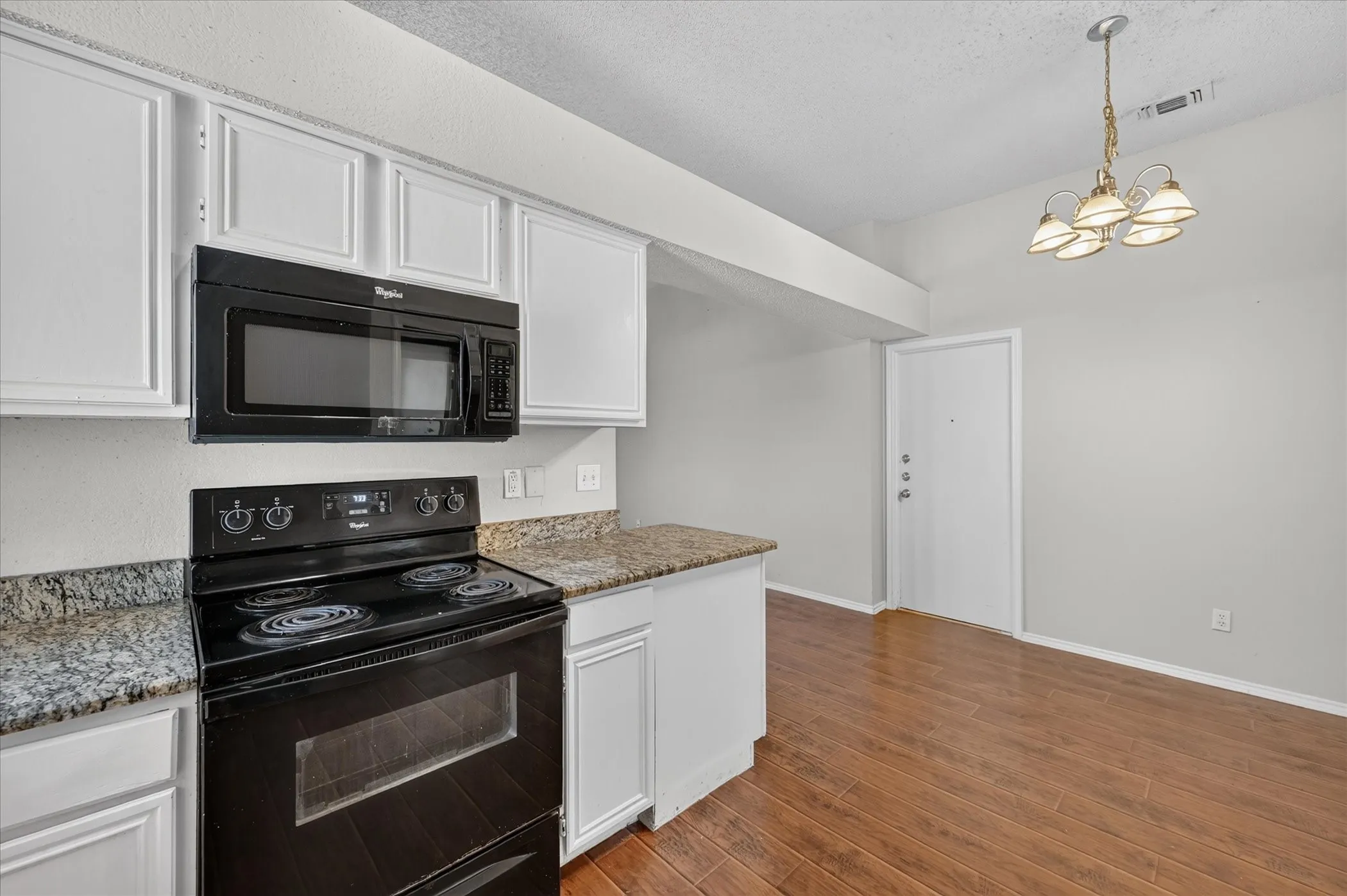 White cabinetry with black hardware, stone-finish countertops, black built-in microwave, and wood-finish flooring