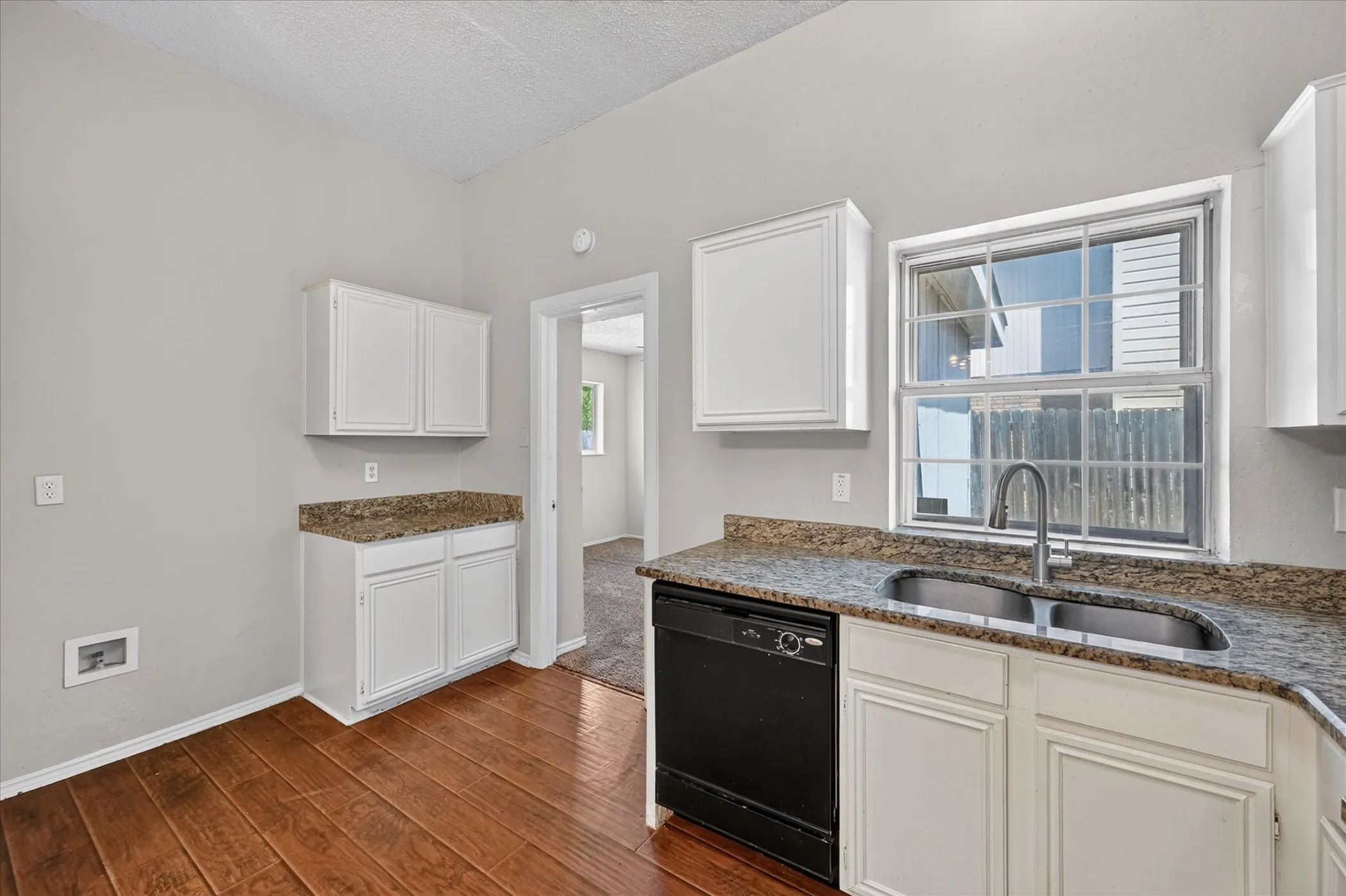 White cabinetry, wood-finish flooring, dual basin sink, black dishwasher, and granite-look countertops