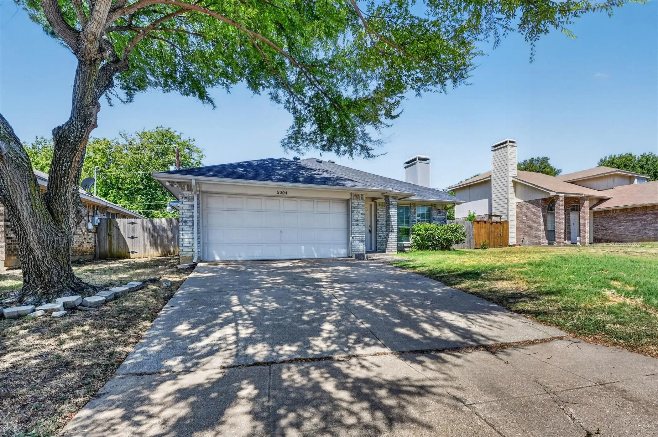 Brick veneer exterior with an attached garage, a concrete driveway, and a fenced side yard