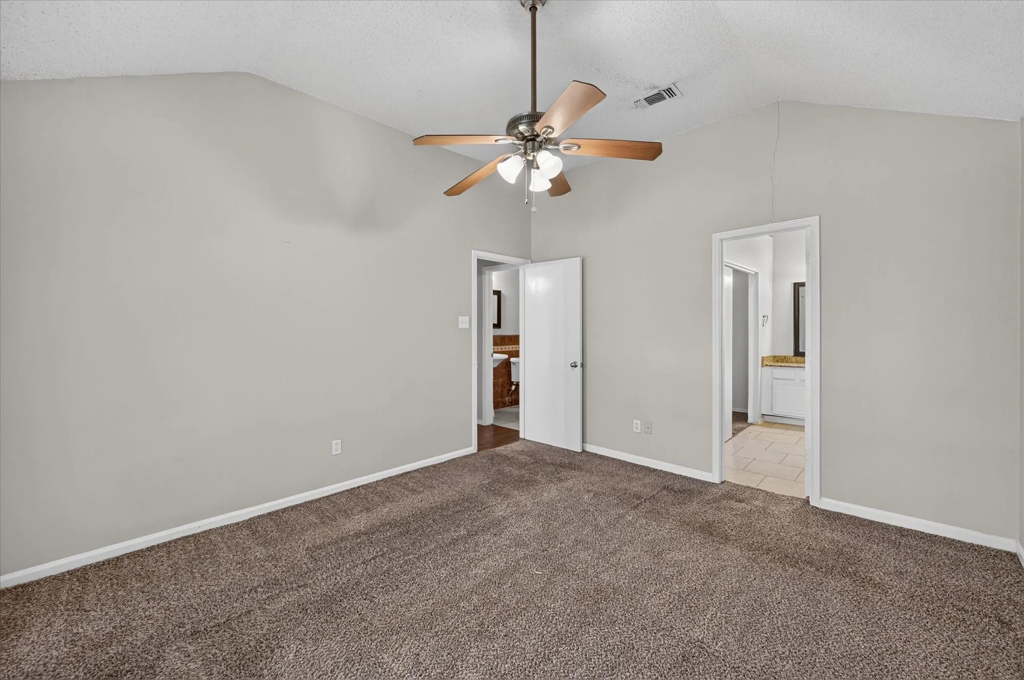 Vaulted ceiling, ceiling fan with light fixture, gray painted walls, brown carpet flooring