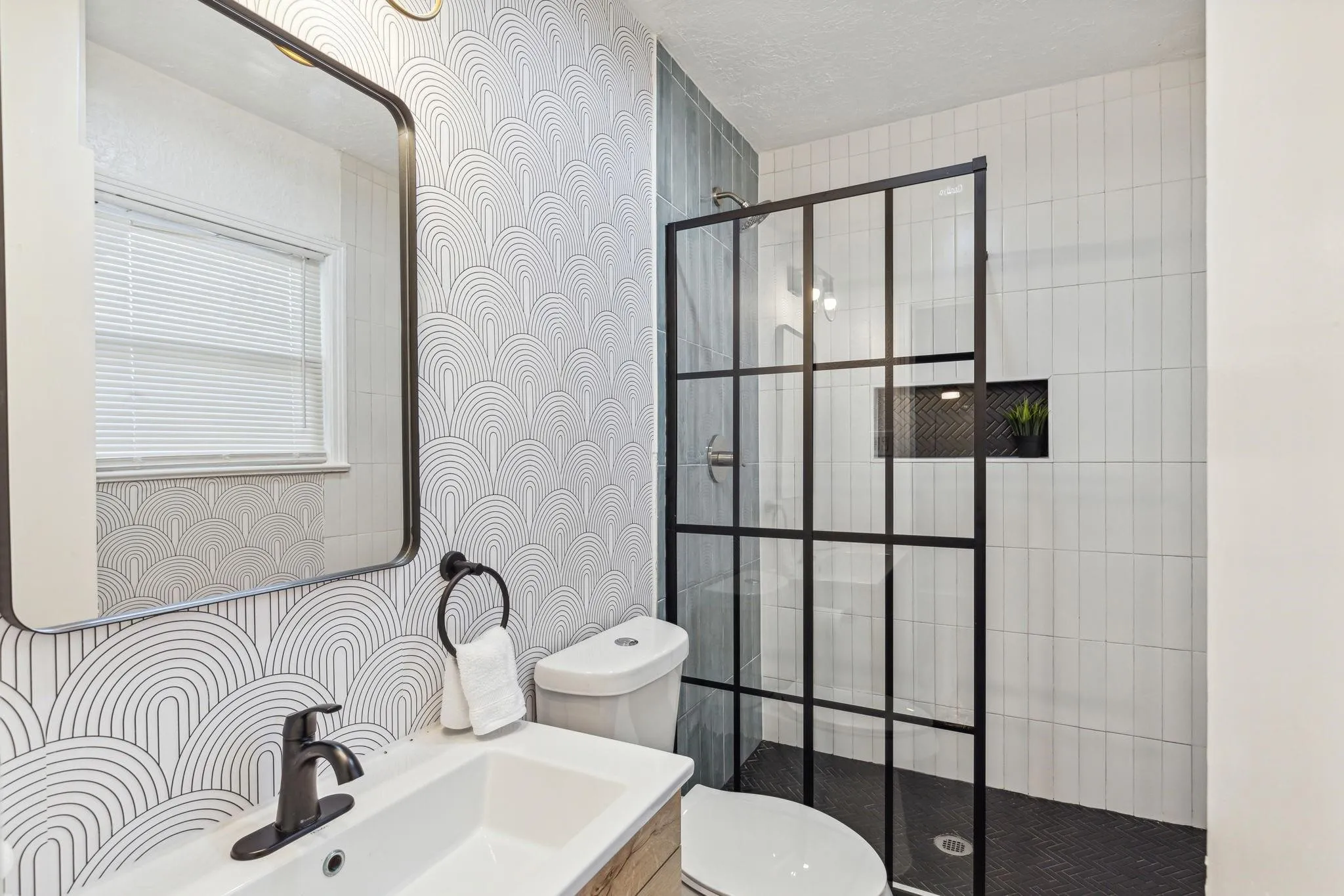 Modern bathroom featuring a vanity with a rectangular sink, black-framed mirror, and a walk-in shower with a black grid-patterned glass enclosure